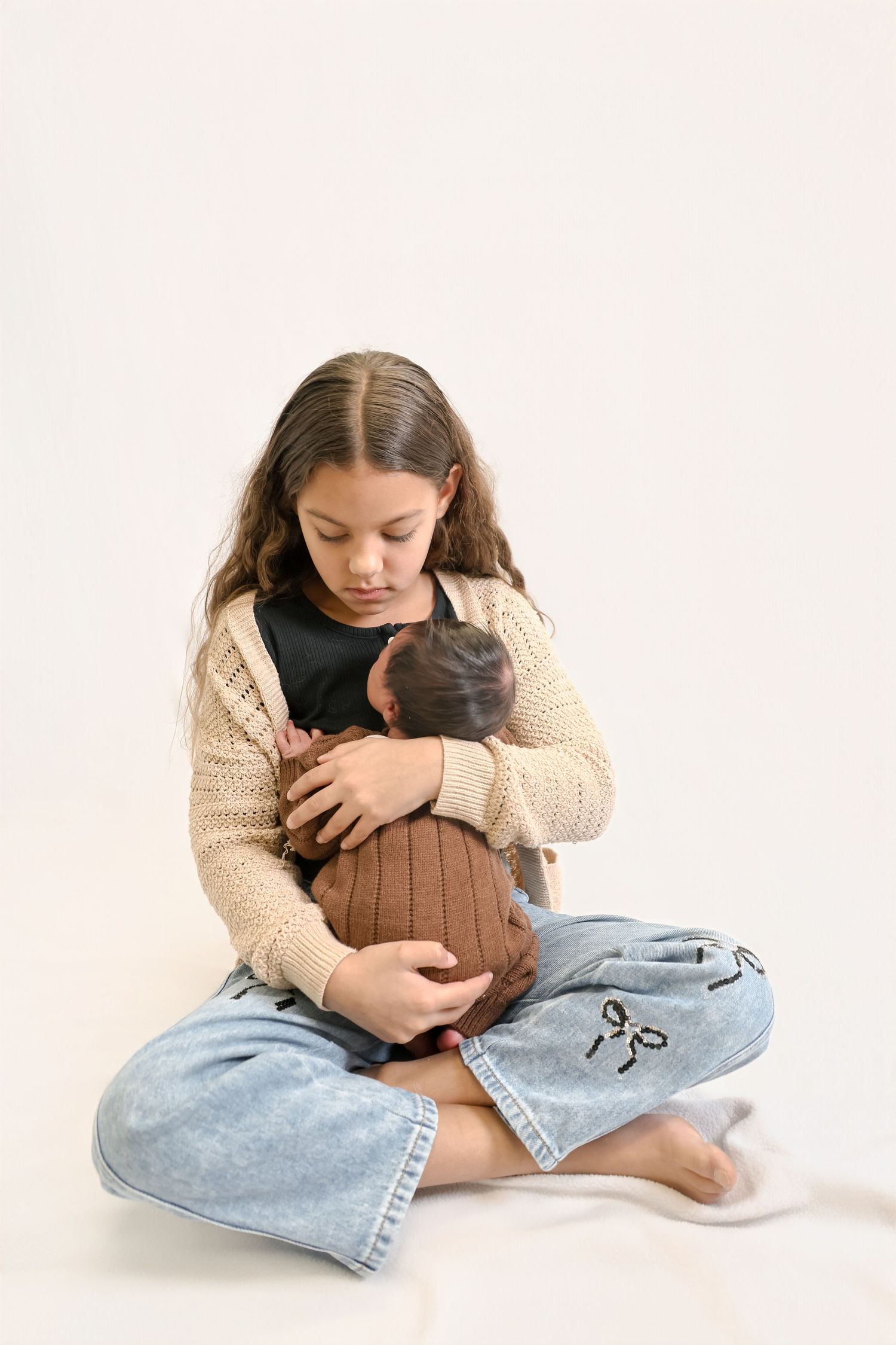 A person wearing a cream sweater and jeans sits cross-legged while cuddling a small brown cat in three sequential photos.