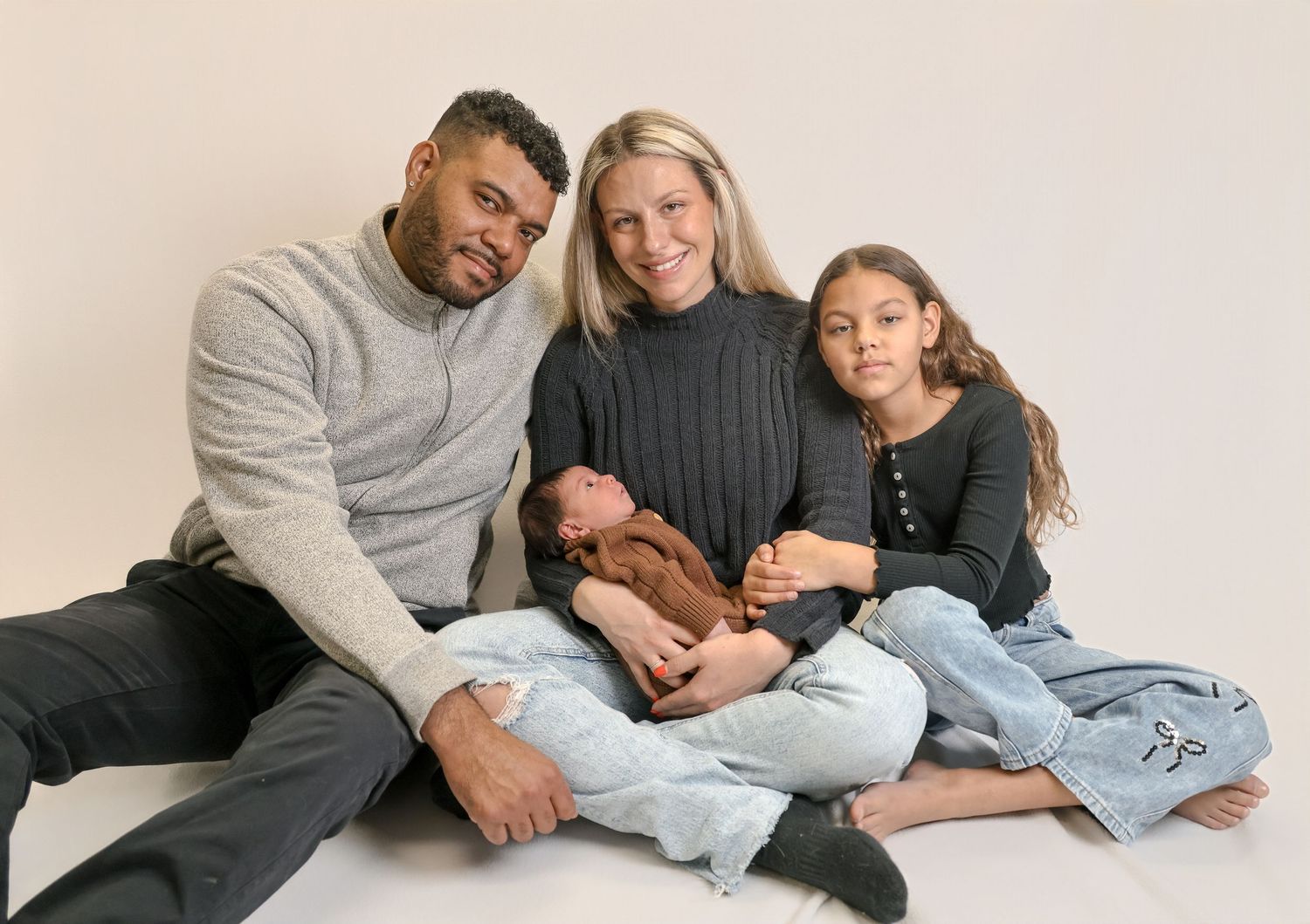 A family in coordinating gray outfits lounges together on a white background in a series of candid poses.