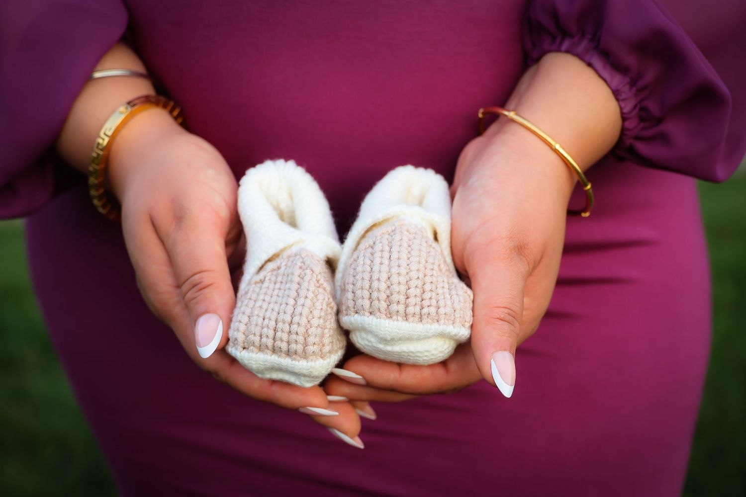 Hands holding small white knitted baby booties against a purple background.