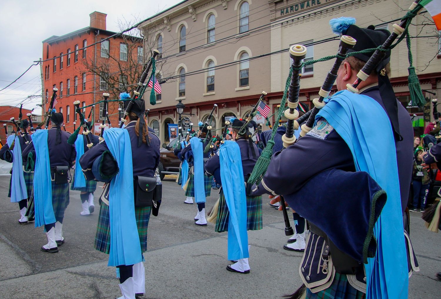 Performers in light blue robes and dark suits participate in a street parade through a historic downtown district.