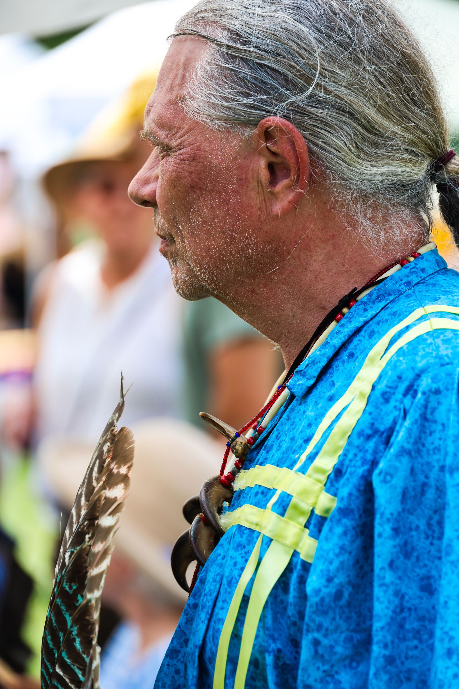 Person wearing a blue jacket with yellow reflective stripes examines a small feather in profile view.