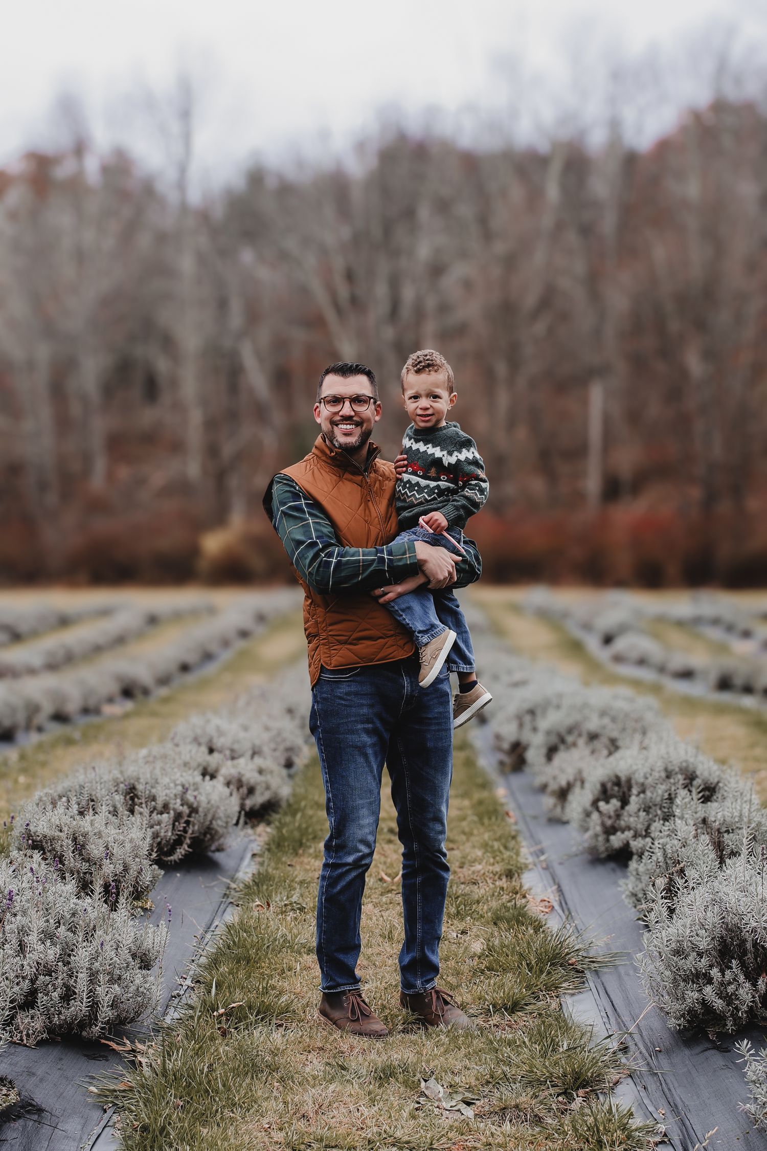 Two people walking together through rows of lavender plants covered with black landscaping fabric on a cloudy day.