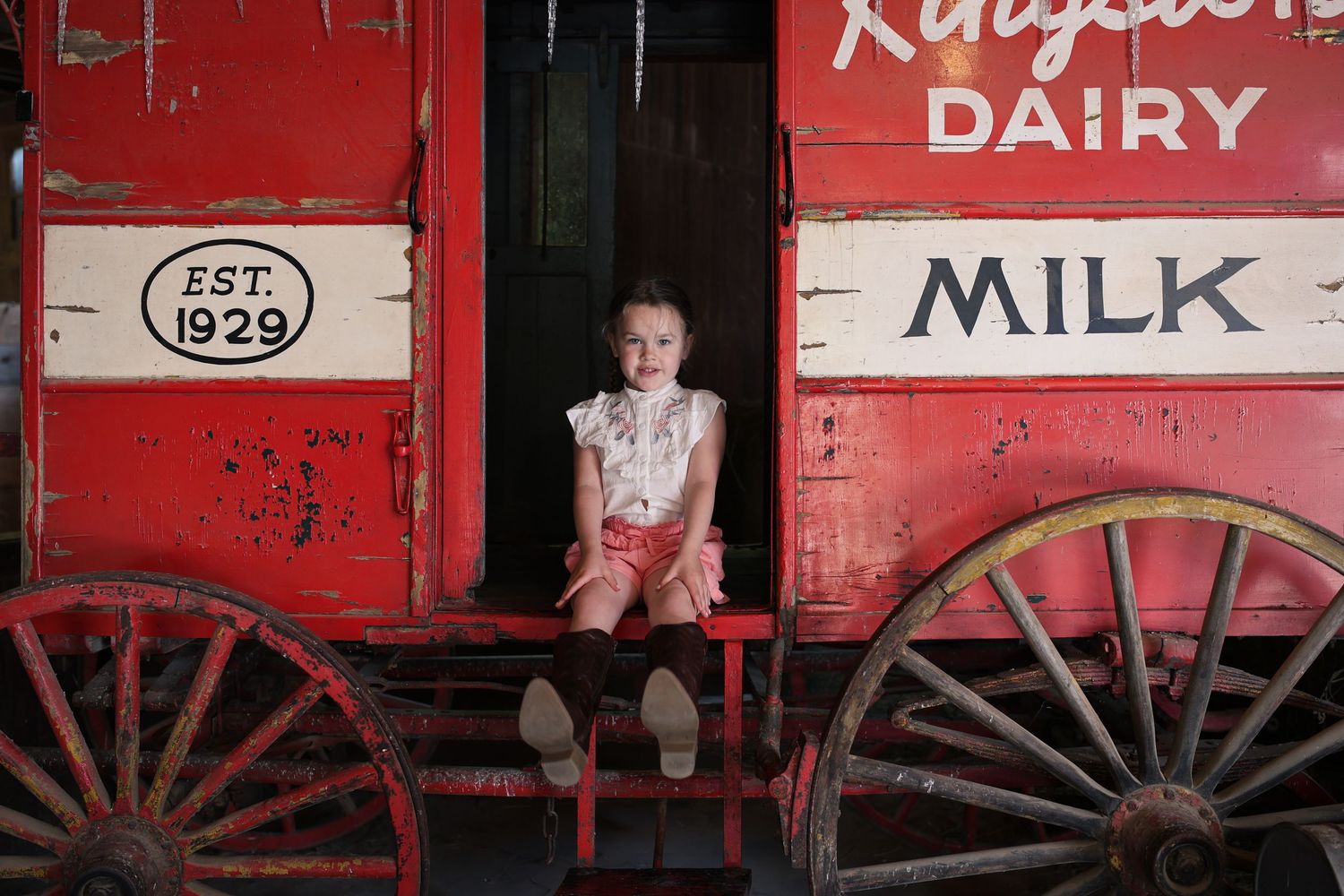 A vintage red dairy wagon from 1929 with wooden wheels sits against a rustic background.