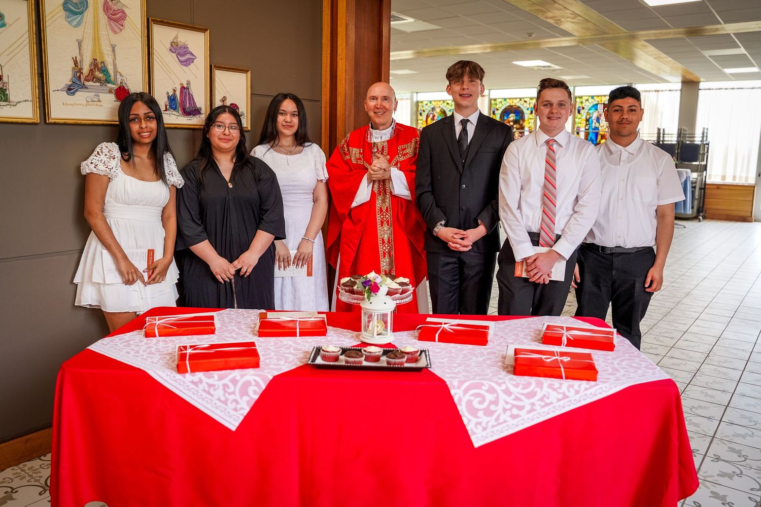 A group of people stand behind a red-clothed table during a signing or celebration event.