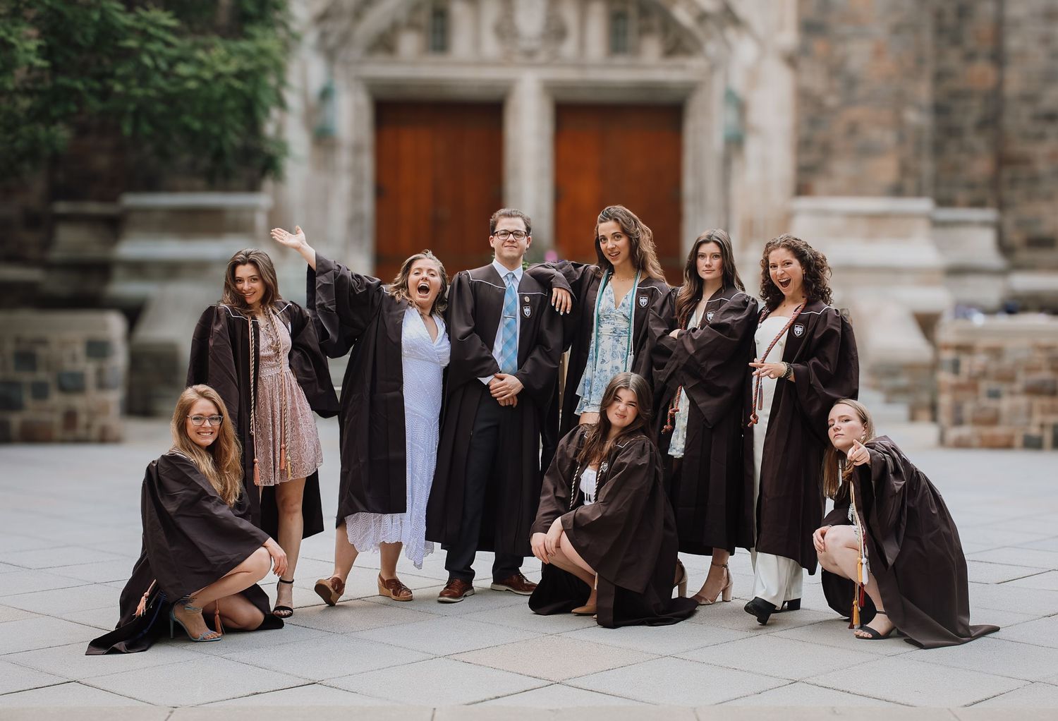 A group in formal attire sits together on stone steps for a stylish outdoor photo session.