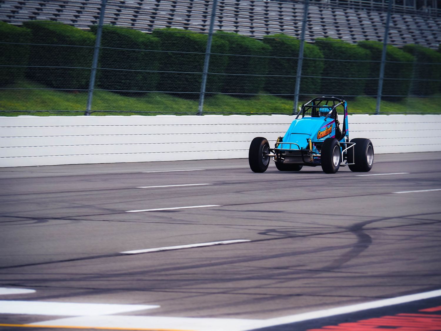 Formula racing cars compete on a racetrack during a motorsport event with white barriers and green surroundings.