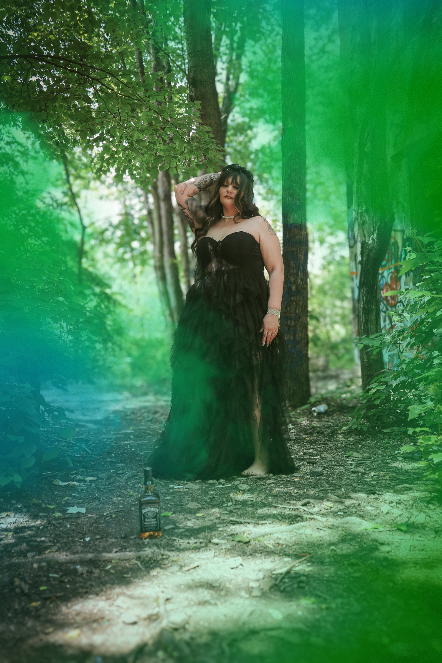 A person in a black dress poses ethereally in a misty green forest setting with dramatic lighting and atmospheric effects.