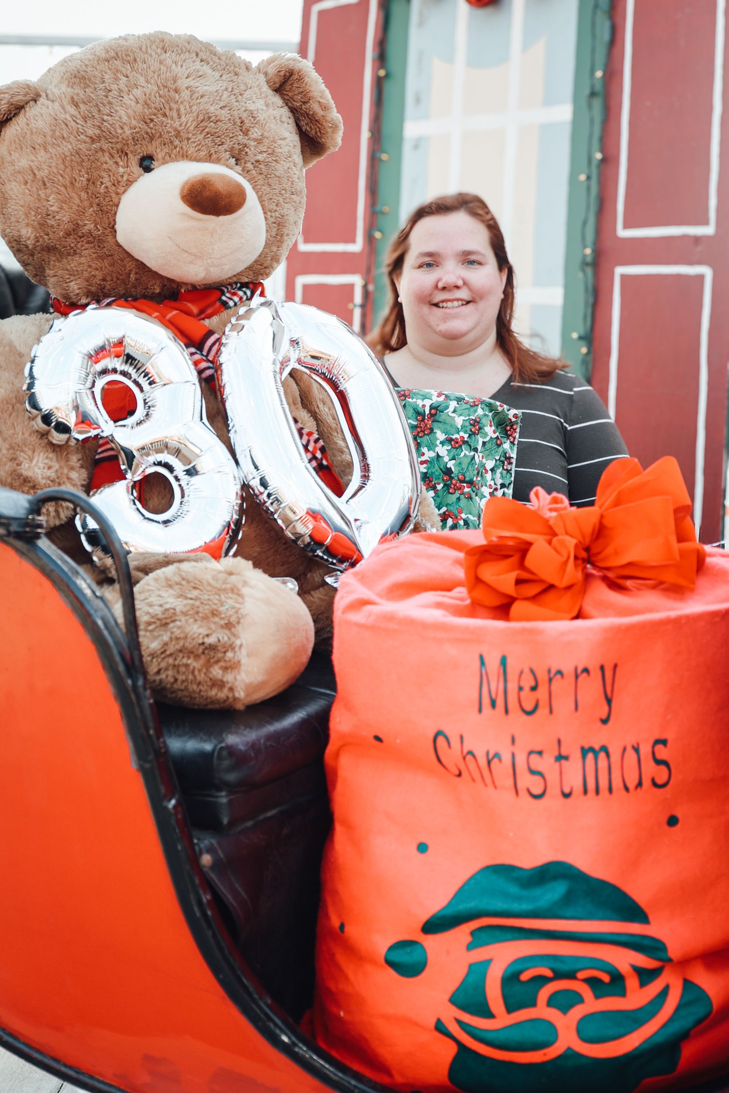 A large teddy bear with silver number 50 balloons sits next to an orange Christmas gift box with decorative designs.