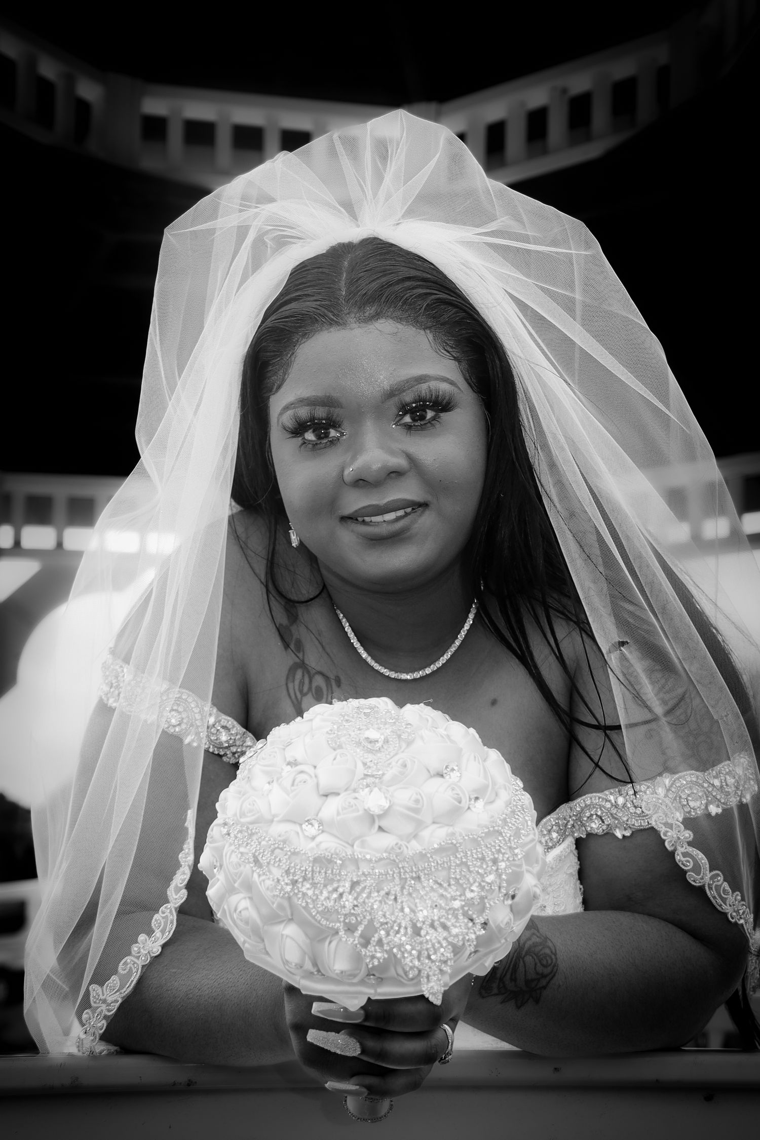 A bride in a white lace wedding dress and veil poses for a series of black and white portraits.