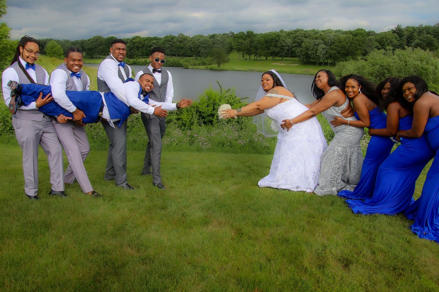 Wedding party in blue and white attire poses playfully in a lush green field on a summer day.