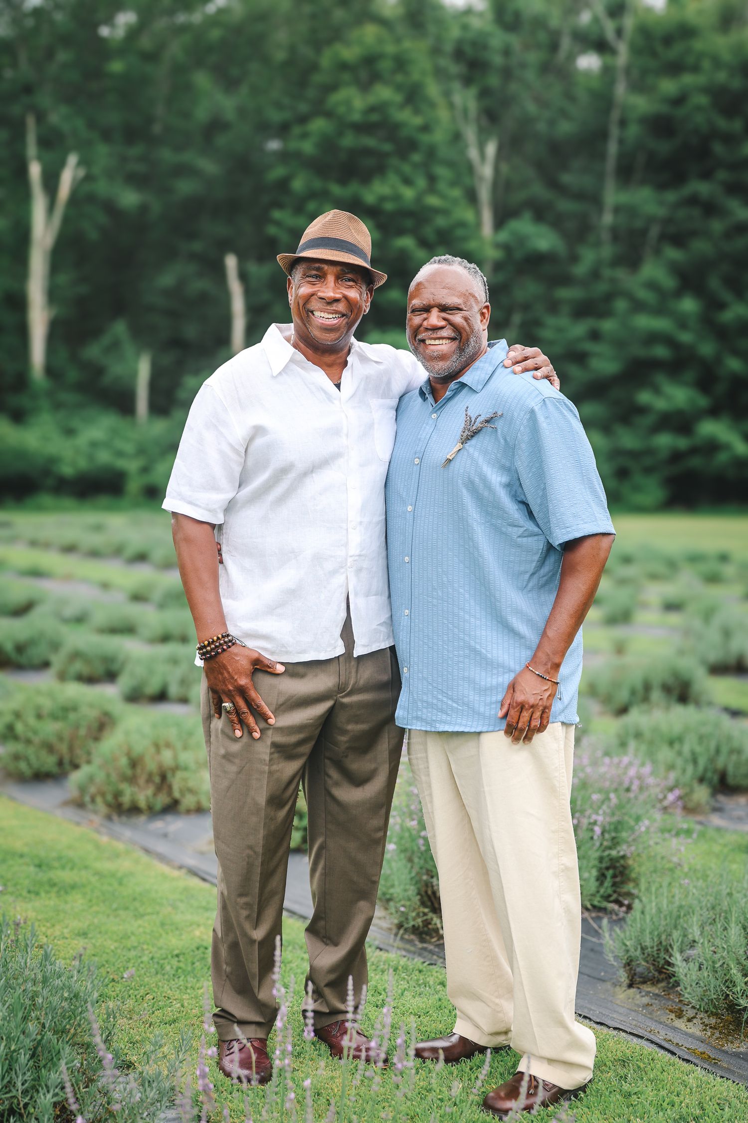 Two men share a warm embrace while standing in a beautiful lavender garden on a sunny summer day.