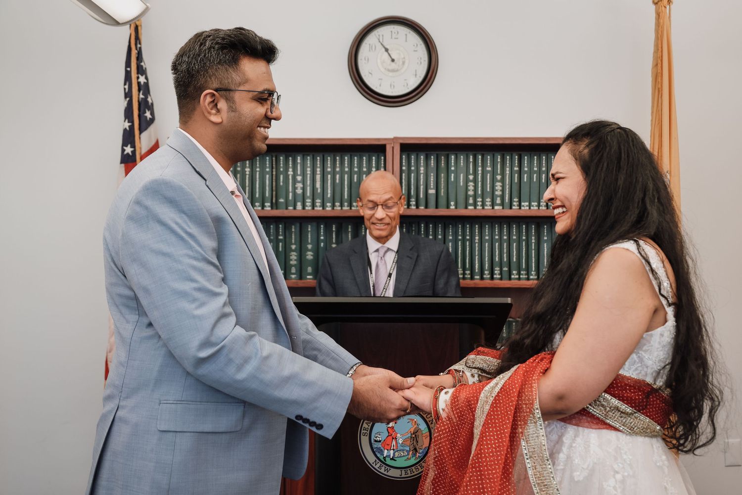 A couple exchanges rings during a courthouse wedding ceremony with a clock visible on the wall.