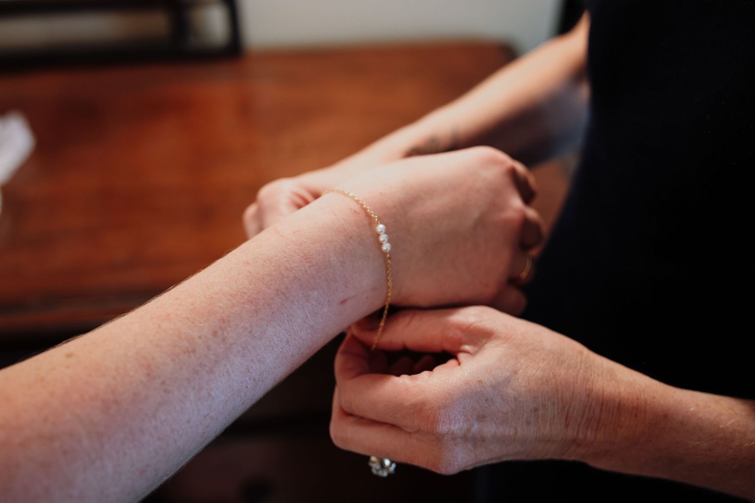 Two hands gently clasp together on a wooden surface with a delicate bracelet visible on one wrist.