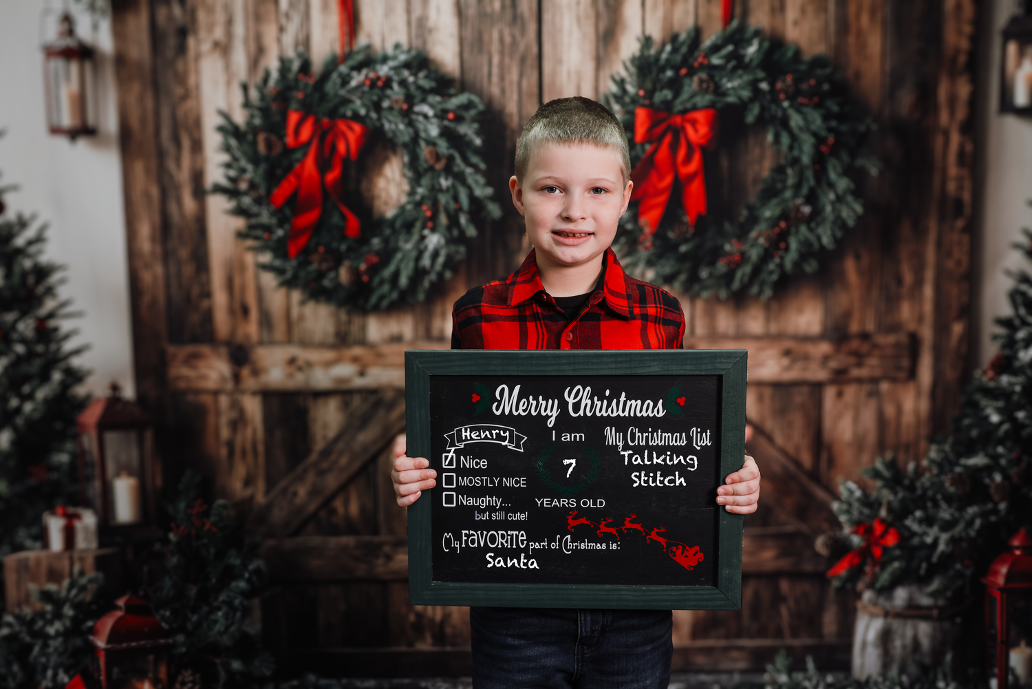 Rustic Christmas photography setup with wooden backdrop, evergreen wreaths and red bows in studio setting.