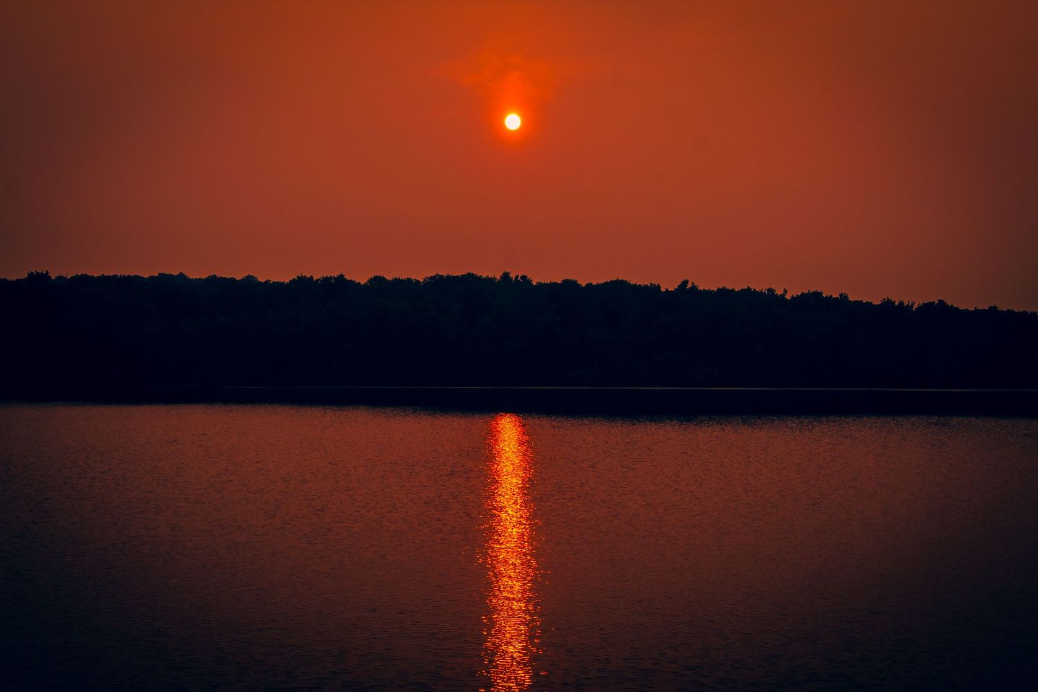 Stunning orange sunset reflection creates a shimmering pathway across the calm lake surface at dusk.