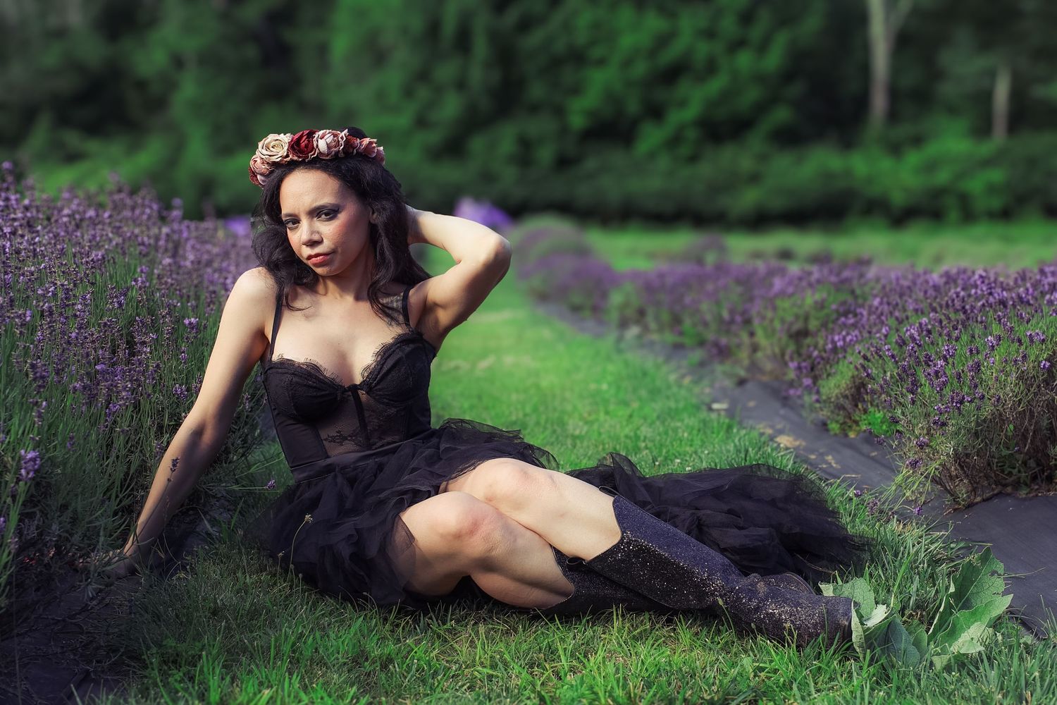 A woman in a black dress poses gracefully in a field of purple lavender flowers on a summer day.