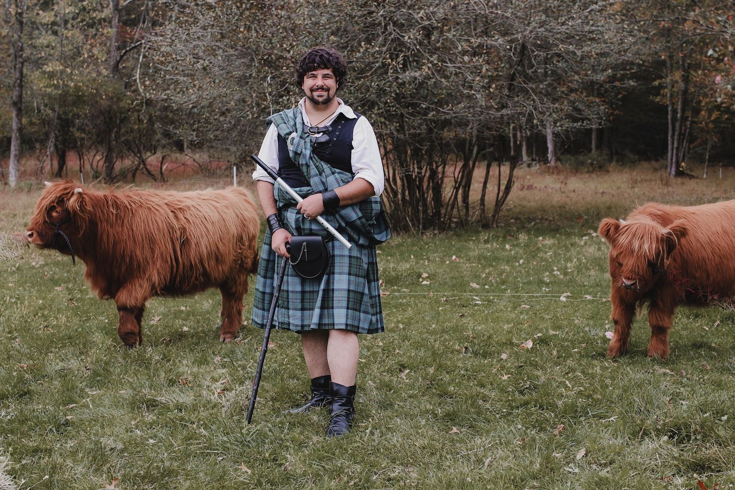 Scottish Highland cattle graze in a grassy field while someone in plaid clothing stands nearby.