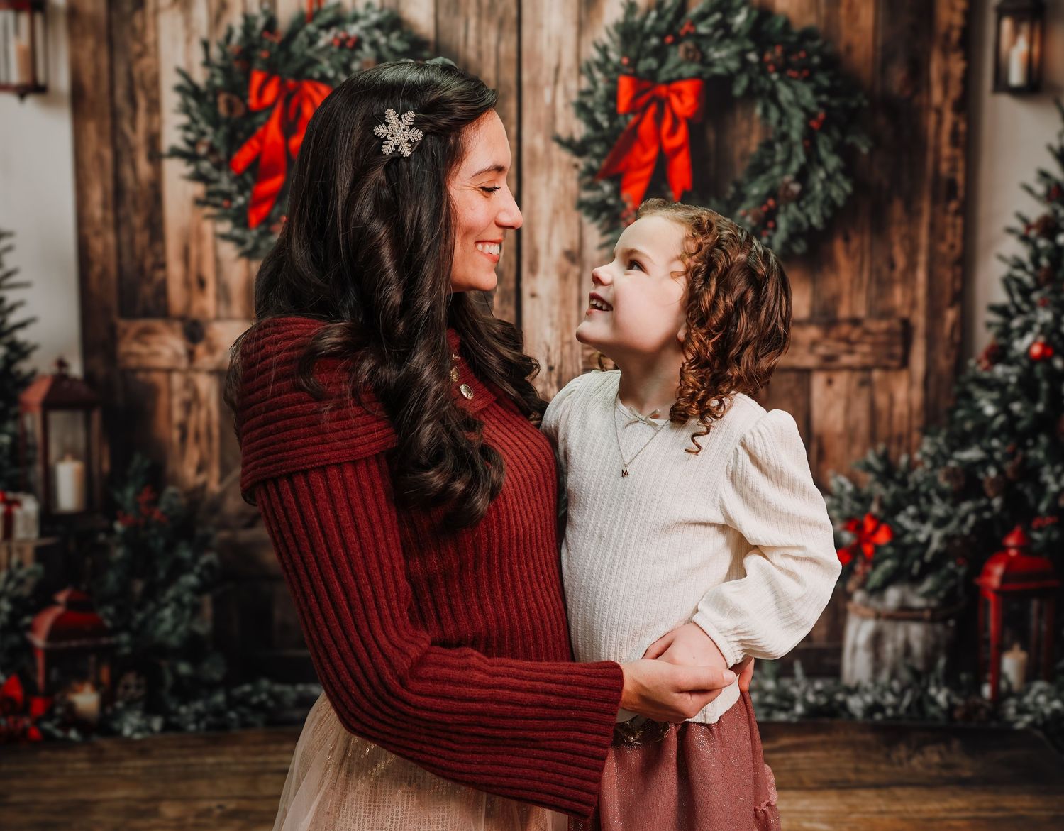 A cozy Christmas photo session with red sweater and holiday wreaths against rustic wooden backdrop.