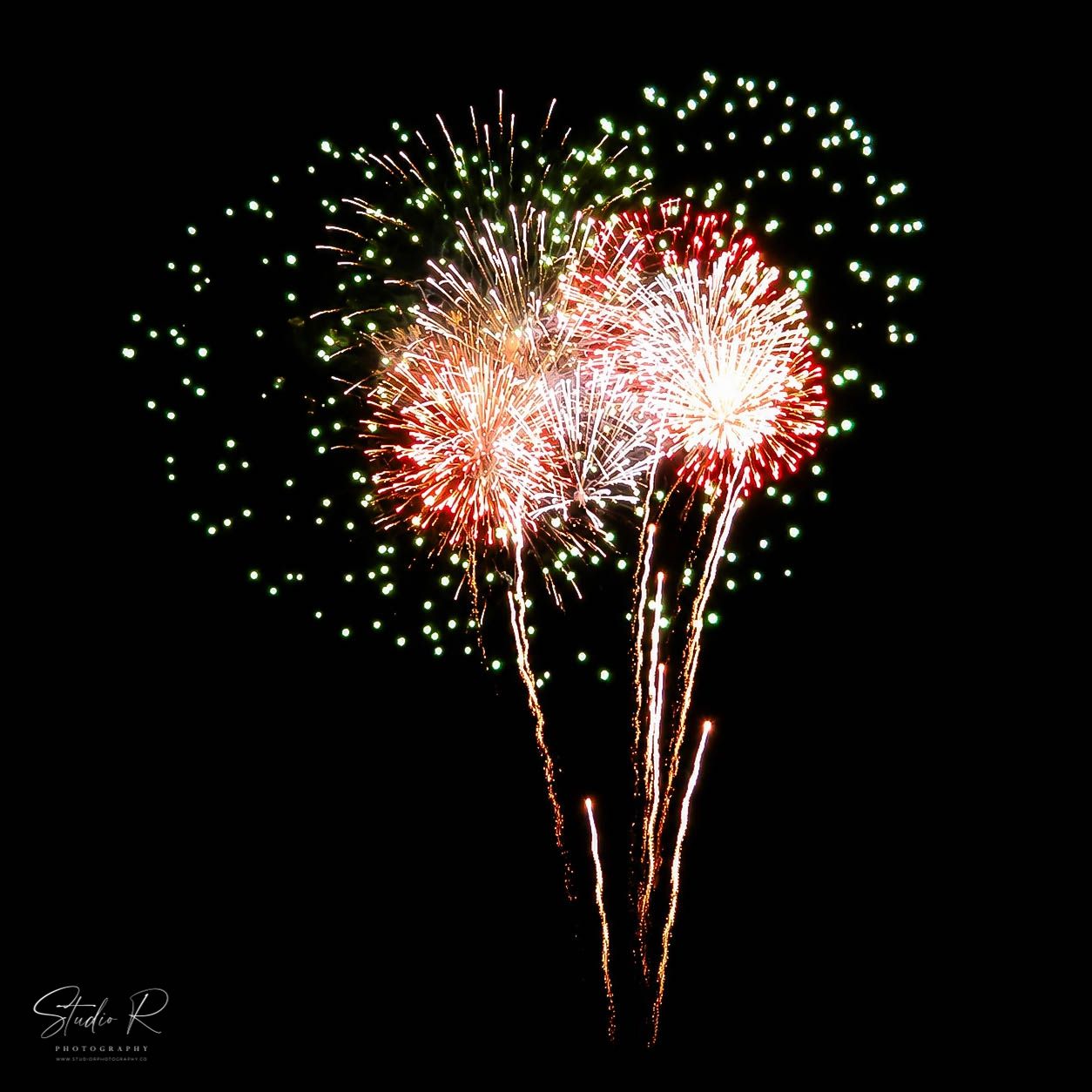 Colorful fireworks display with red, white, and green bursts against a dark night sky.