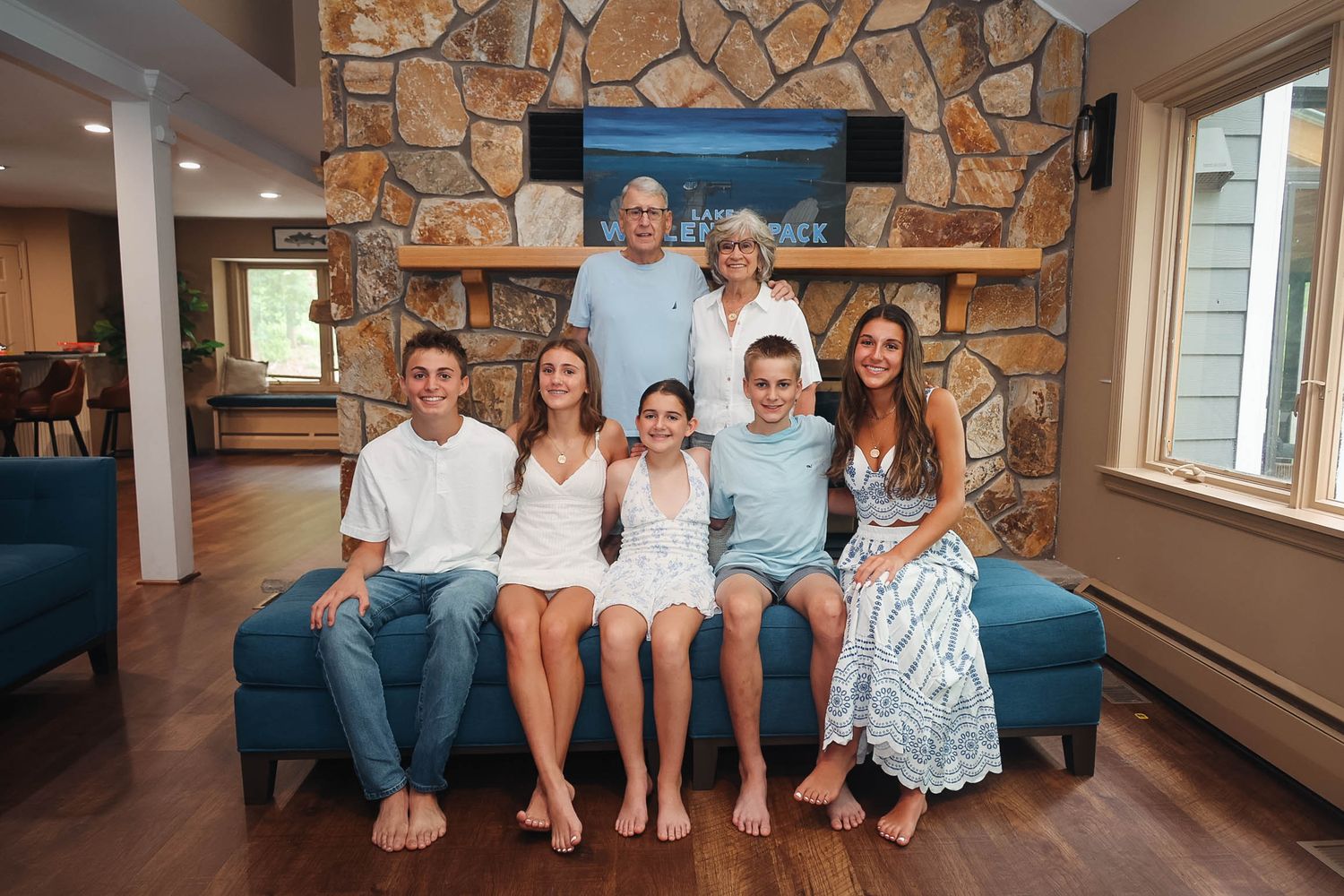 Grandparents and grandchildren smiling together on a blue couch in a cozy stone fireplace living room.