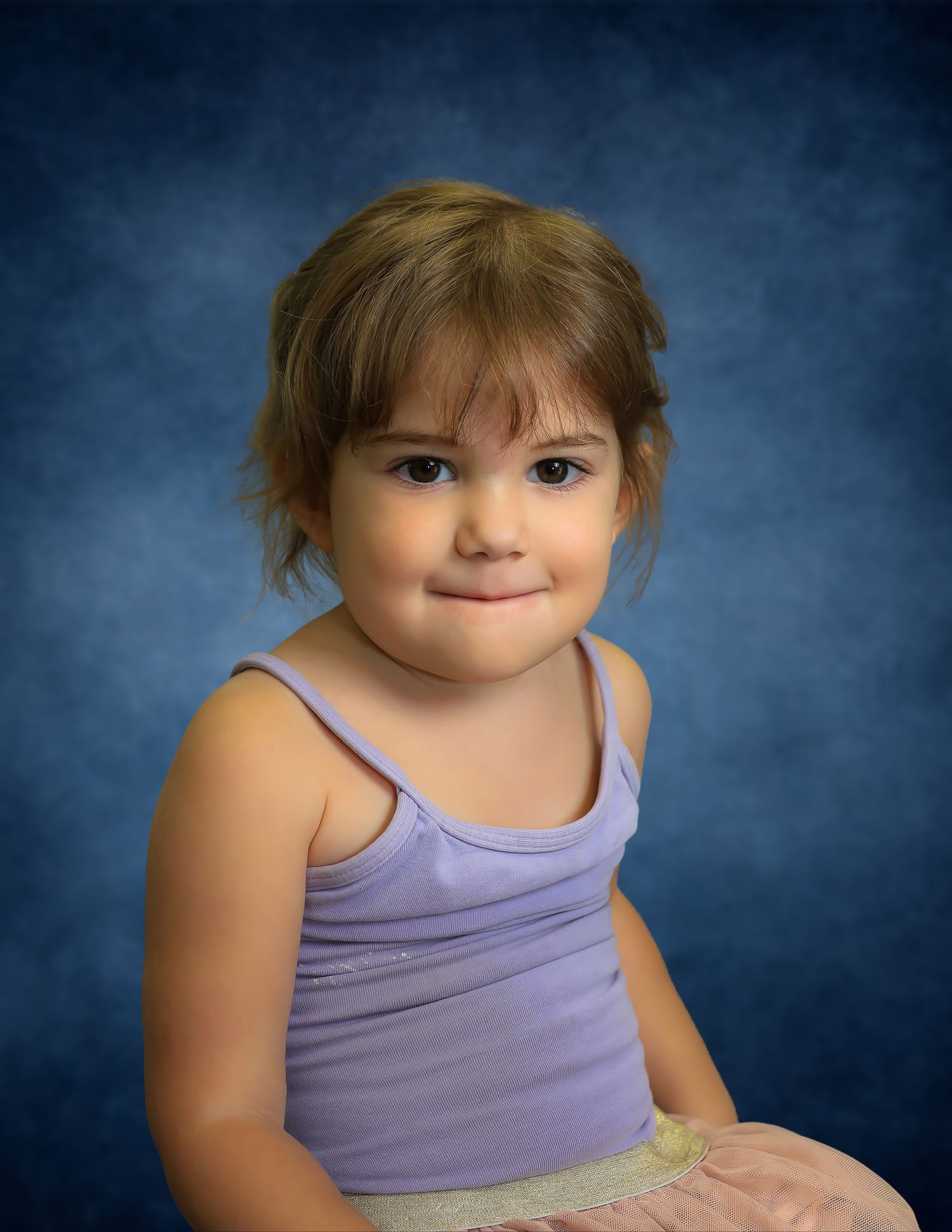 Young girl with brown hair smiling in a purple tank top against a blue studio background.