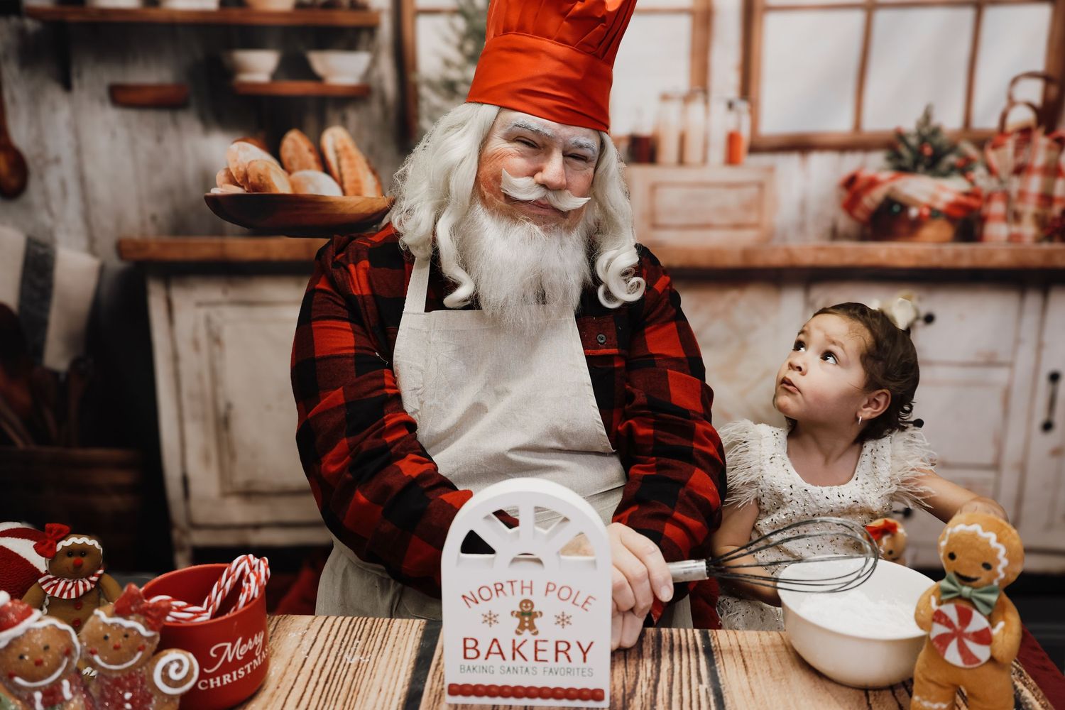 Santa Claus and a young girl baking Christmas cookies together at a North Pole Bakery themed holiday photo session.