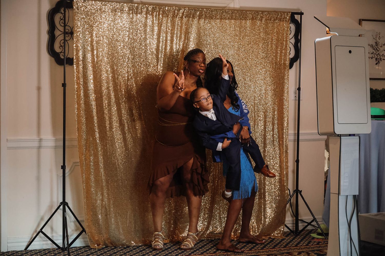 Three women posing playfully in front of a gold sequin backdrop at a photo booth event.