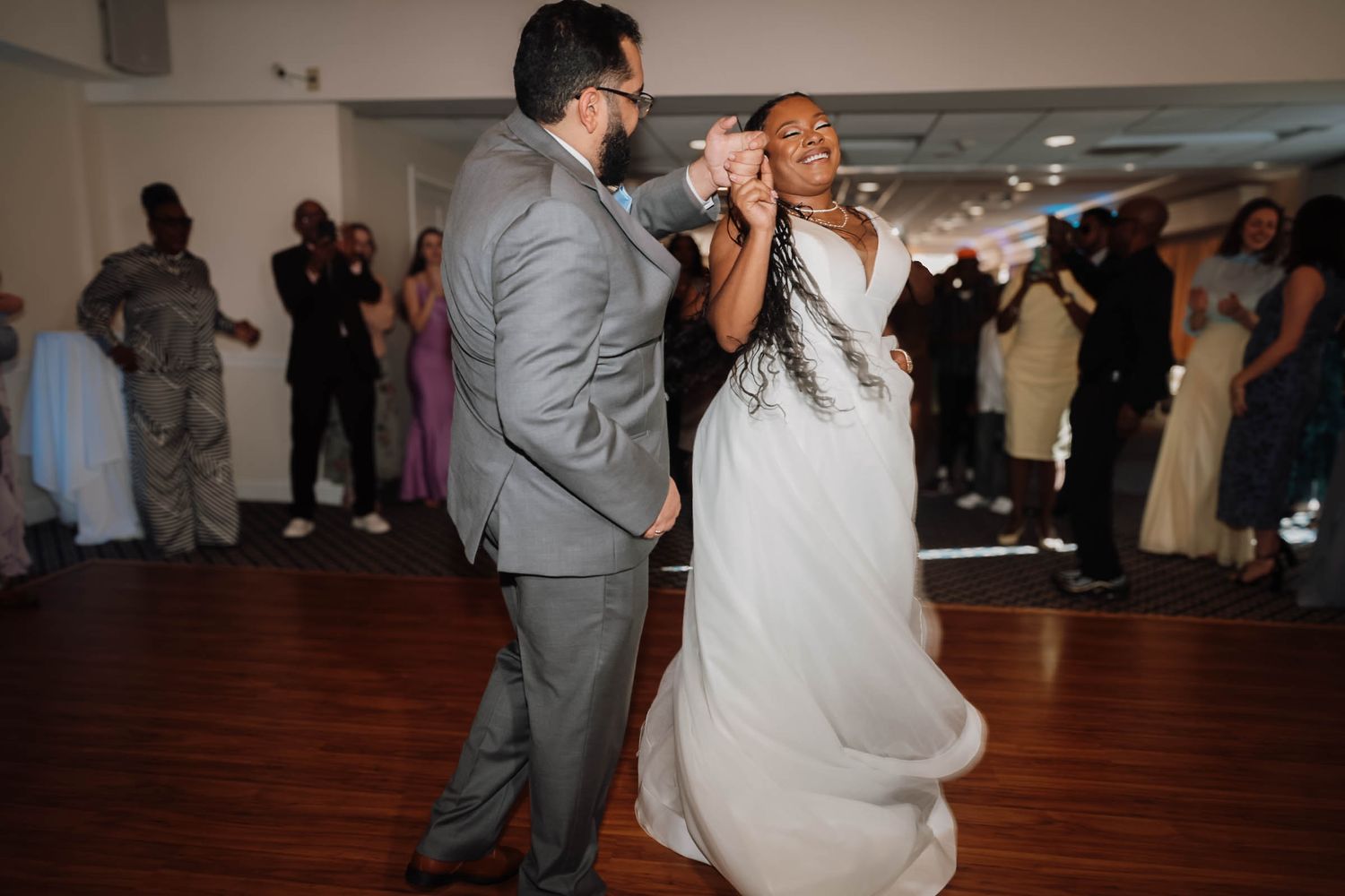 Bride and groom share their first dance at wedding reception, bride in white gown twirling gracefully.