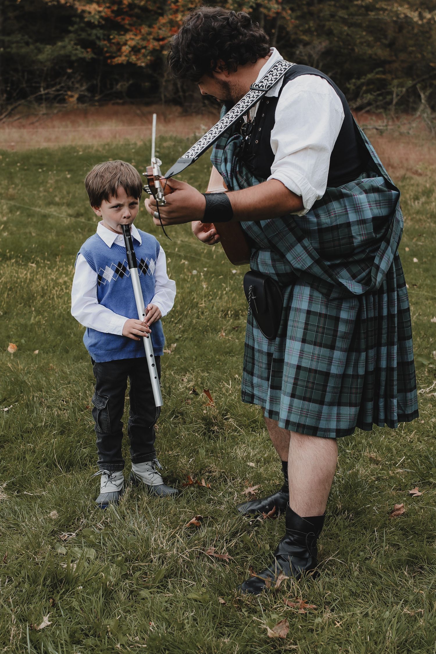 Traditional Scottish music lesson outdoors with bagpipe instructor in kilt teaching young student in blue sweater.