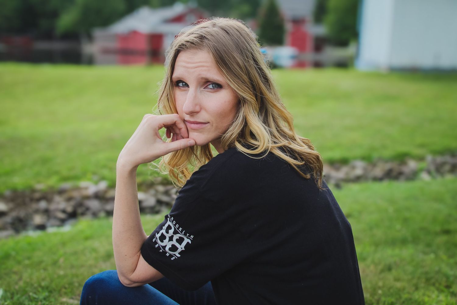 Woman in black sweater sits thoughtfully on grassy lawn during outdoor portrait session.