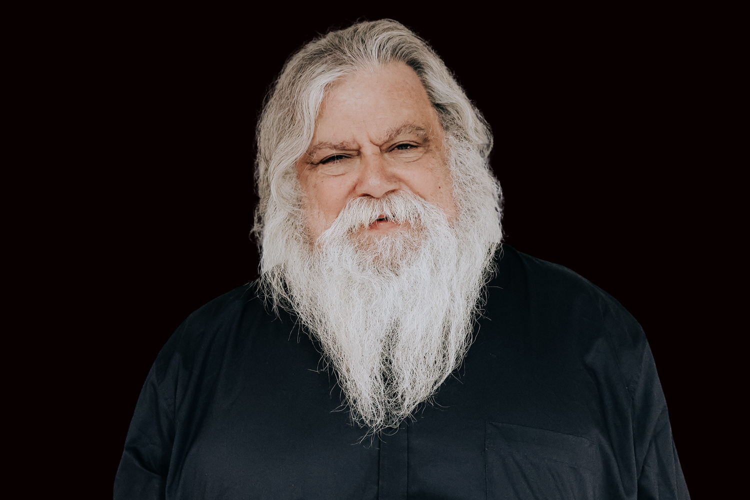 Person with long white beard and dark clothing photographed in multiple poses against black background.