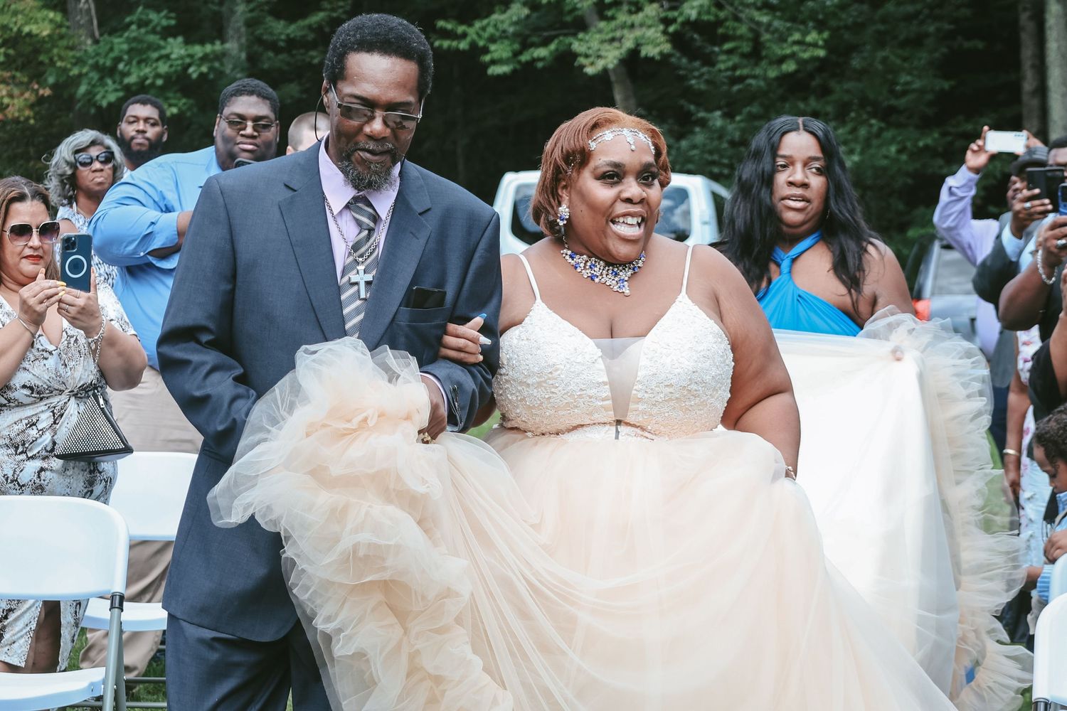 A joyful couple walks down the aisle at an outdoor wedding ceremony while guests smile and celebrate.