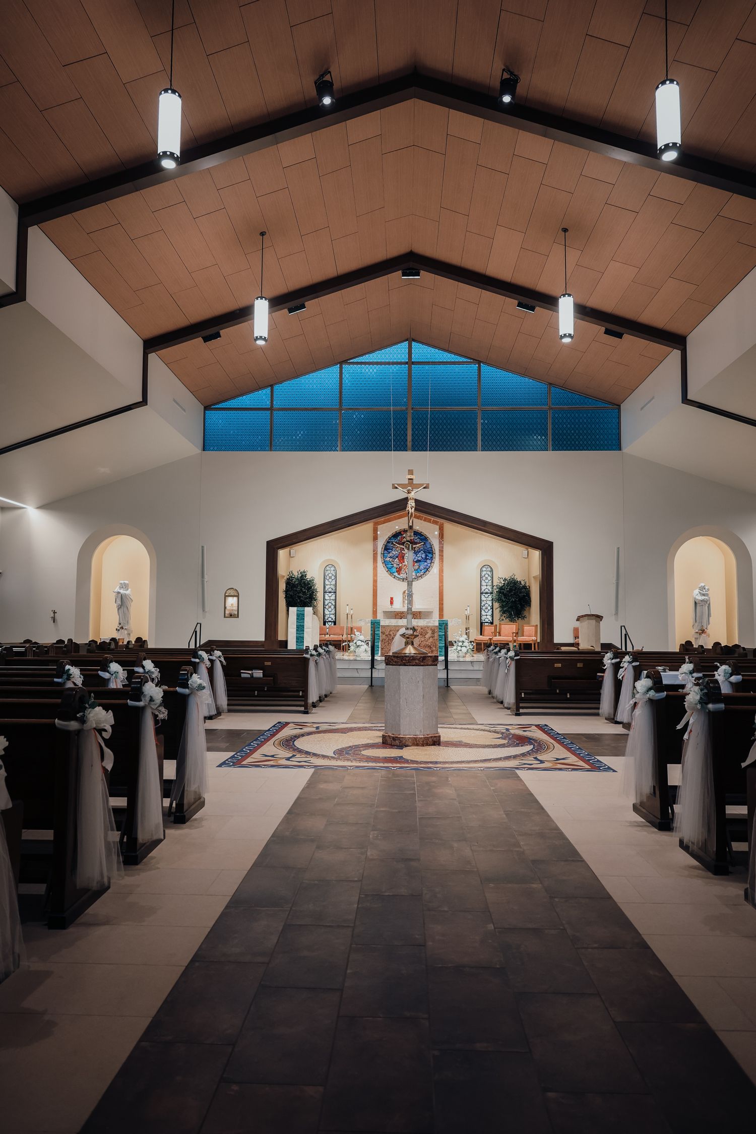 Interior panoramic view of a modern church sanctuary with wooden pews and vaulted ceiling with hanging pendant lights.