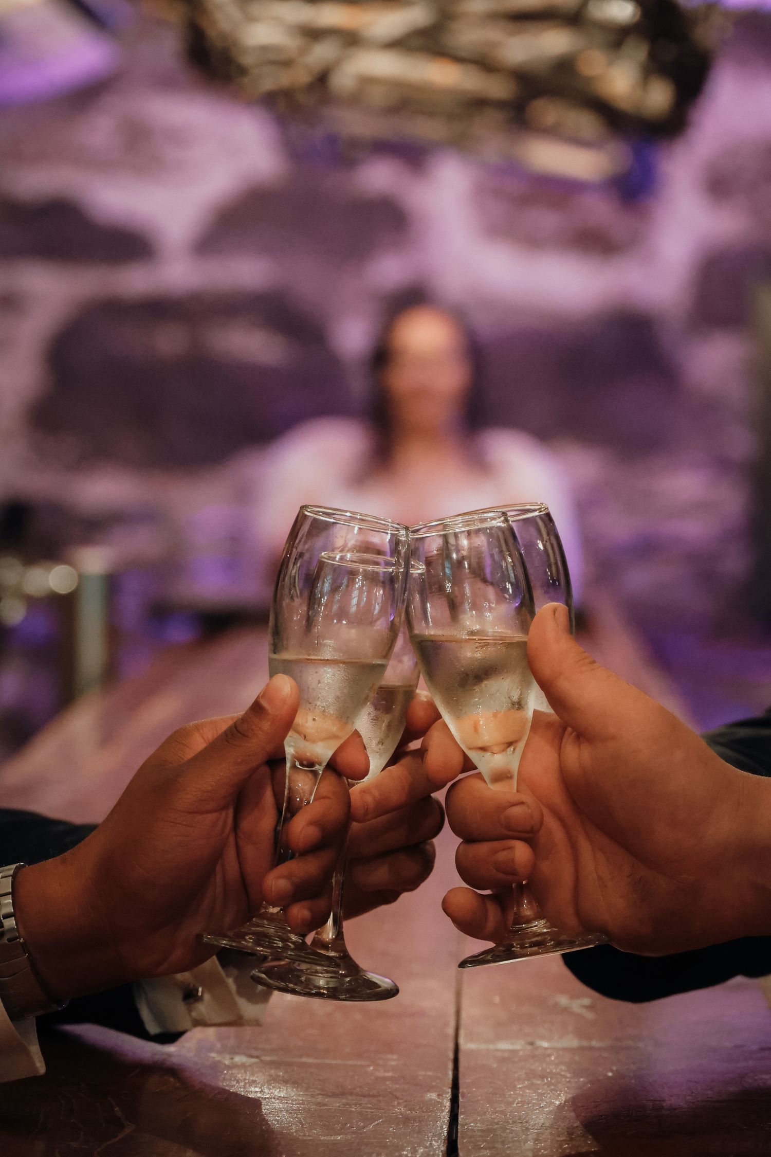 Hands raise champagne glasses in a celebratory toast with purple ambient lighting in the background.