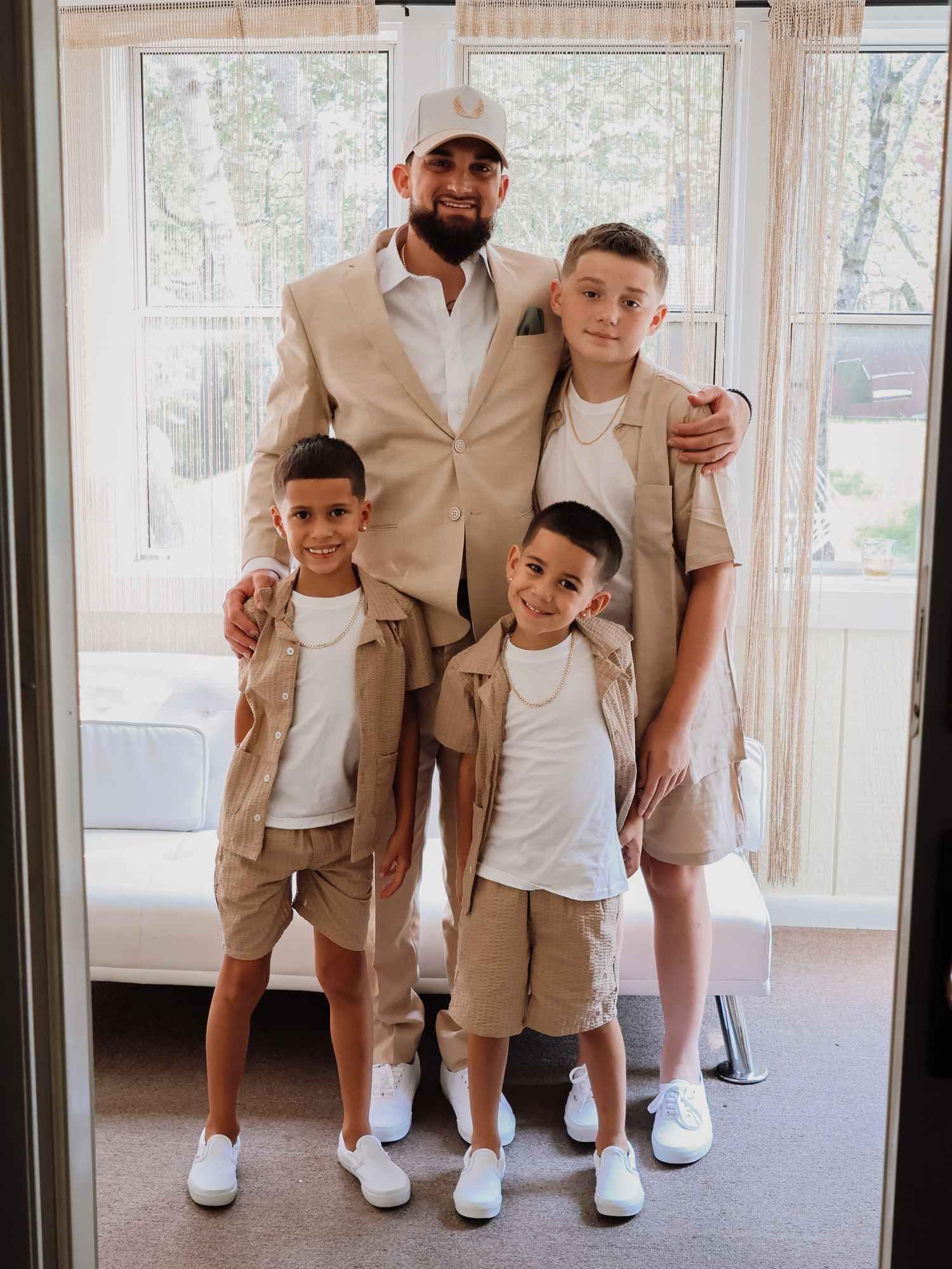 Four people in coordinated beige and white outfits pose together in front of bright windows.