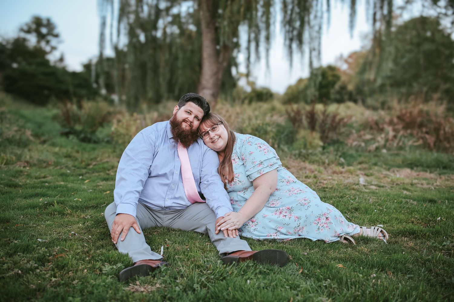 A couple lies together on grass during an outdoor photo session in a natural setting.