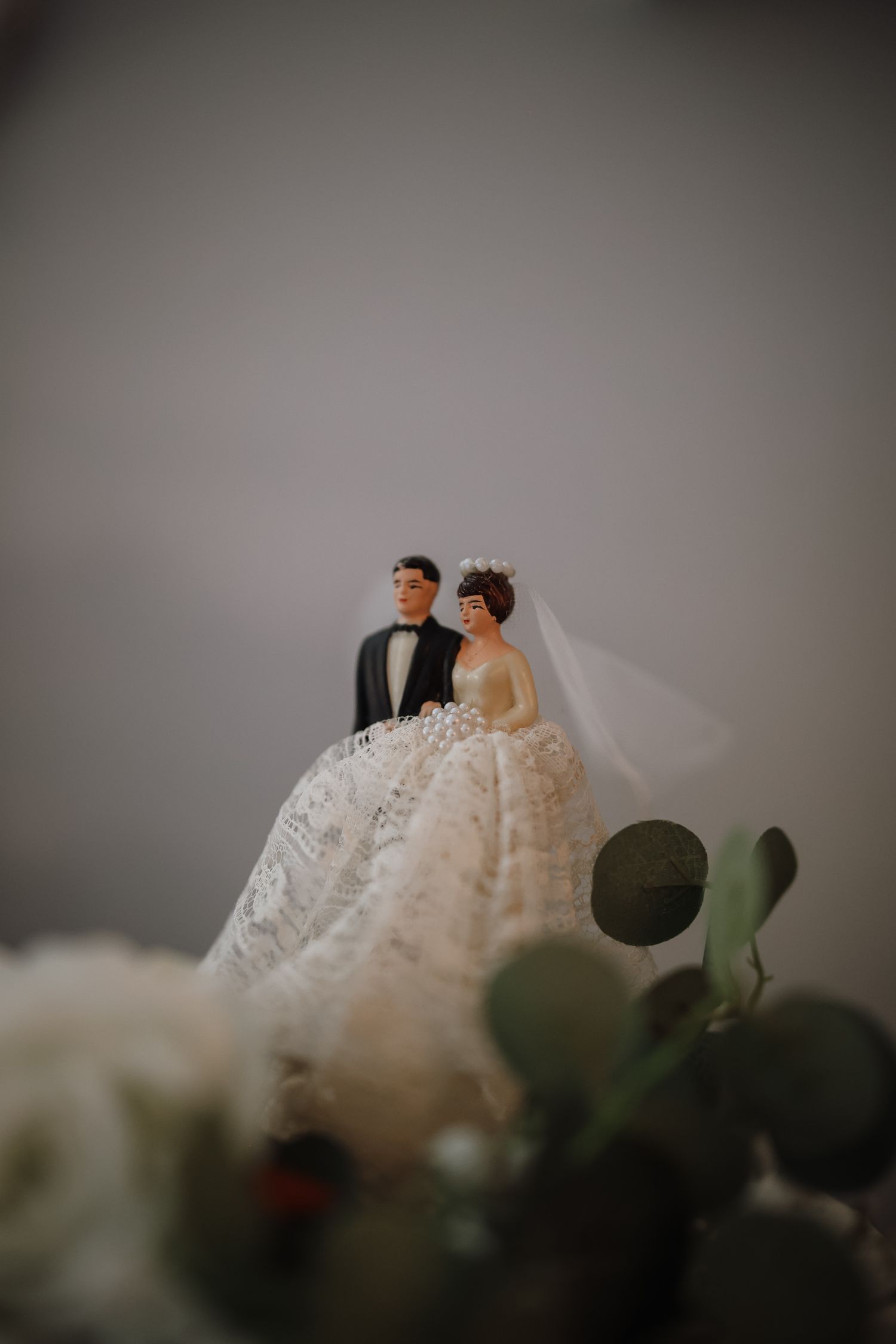 Decorative wedding cake topper figurines displayed with blurred greenery.