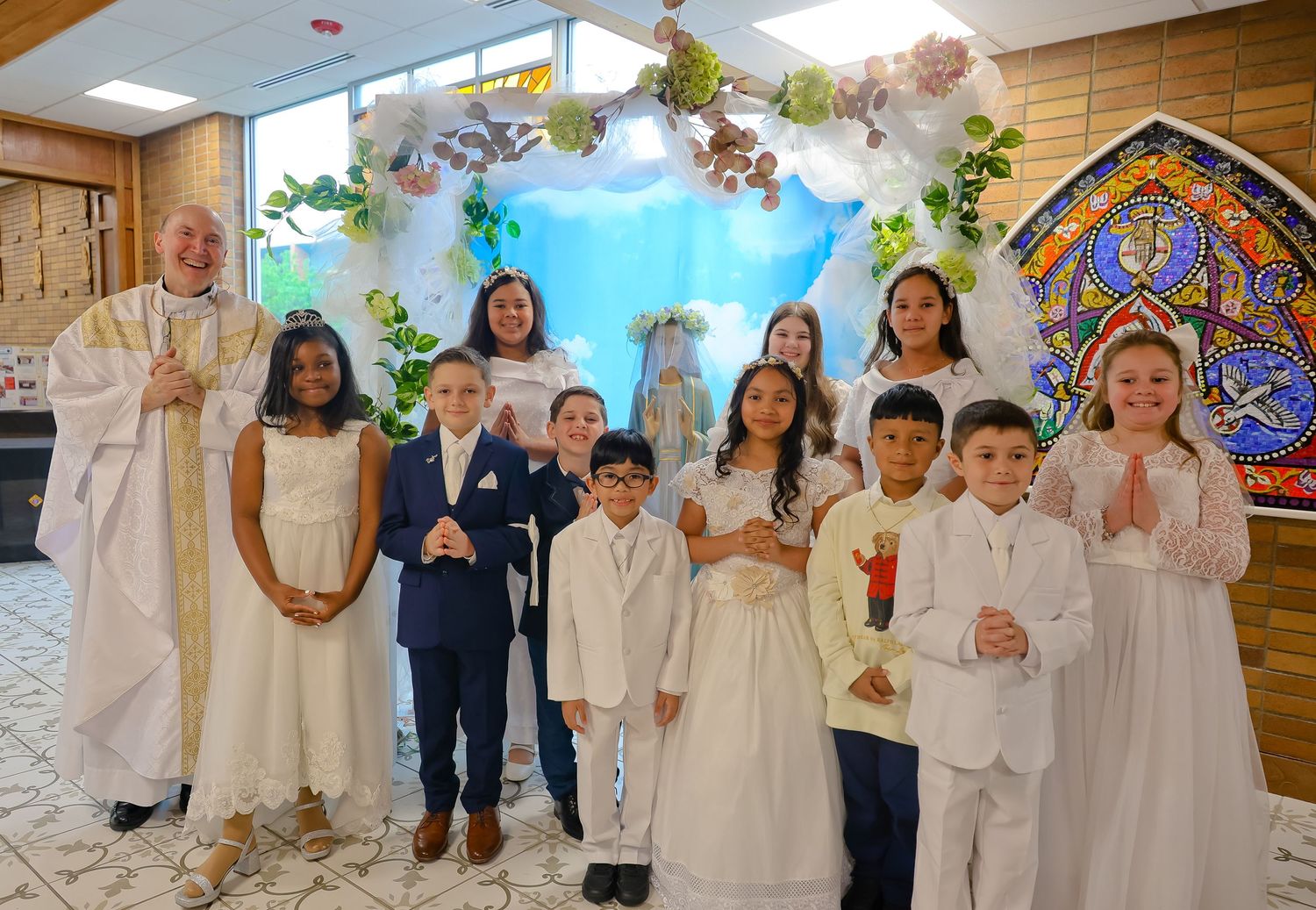 Group of children in white formal attire lined up for a special event celebration.