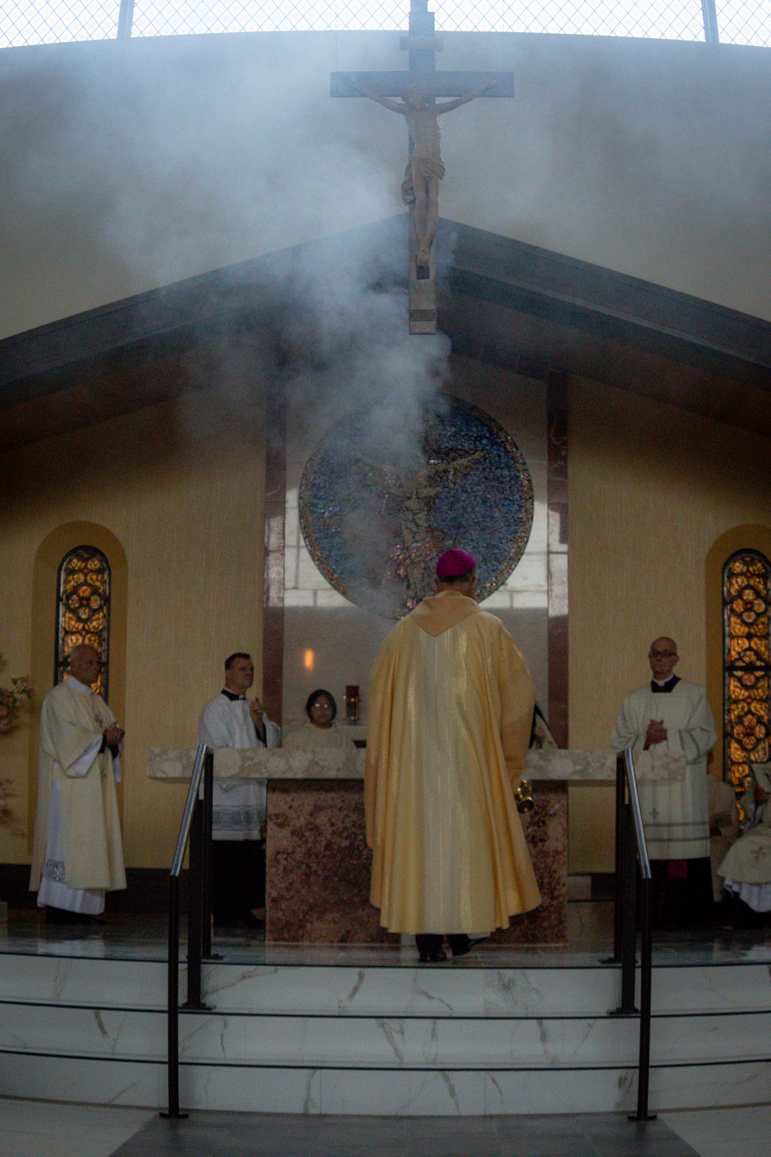 A sequence of Catholic mass ceremony photos showing priests at the altar with incense smoke rising in a church setting.