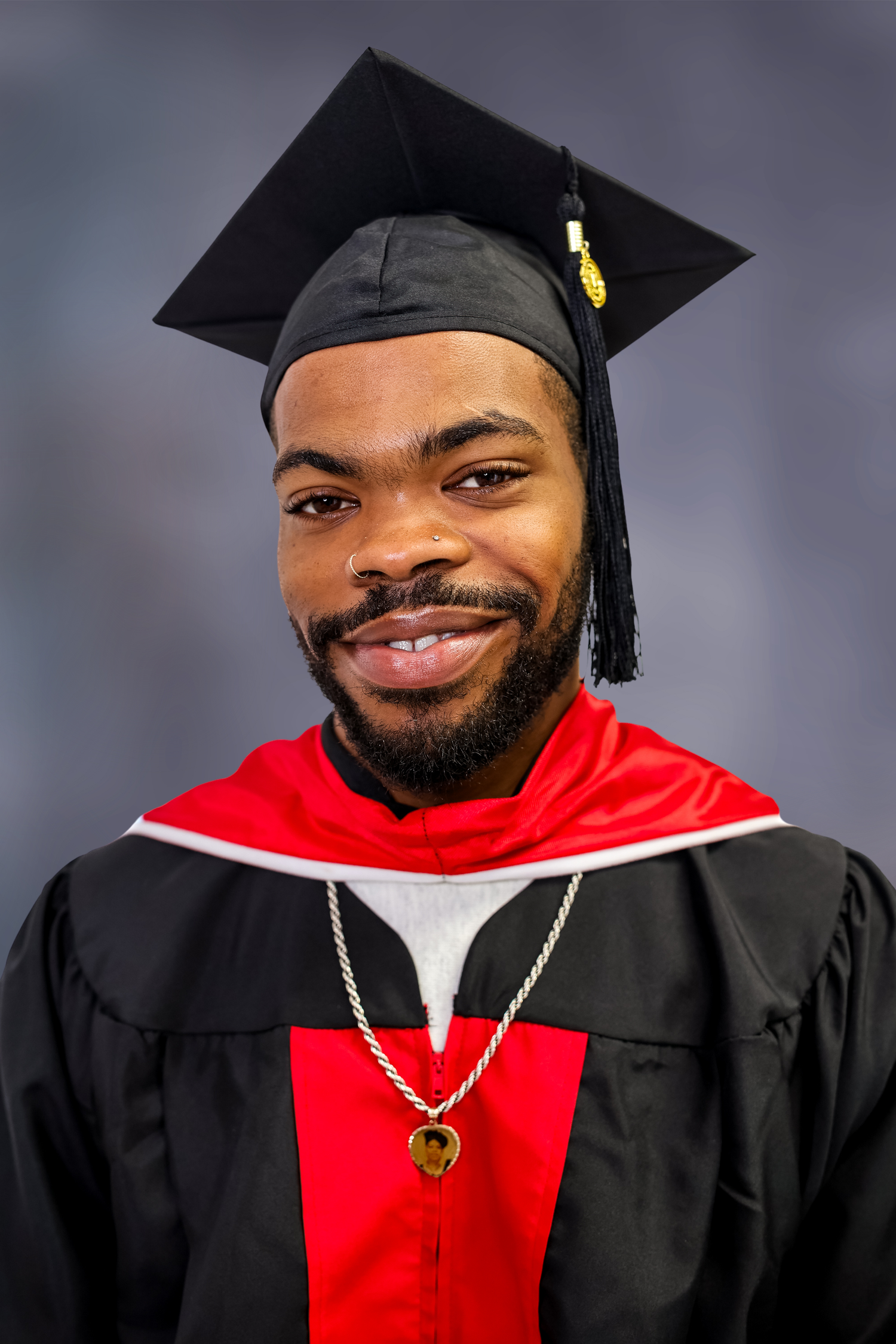 Graduate wearing black and red academic regalia with mortarboard cap and gold tassel smiles at camera.