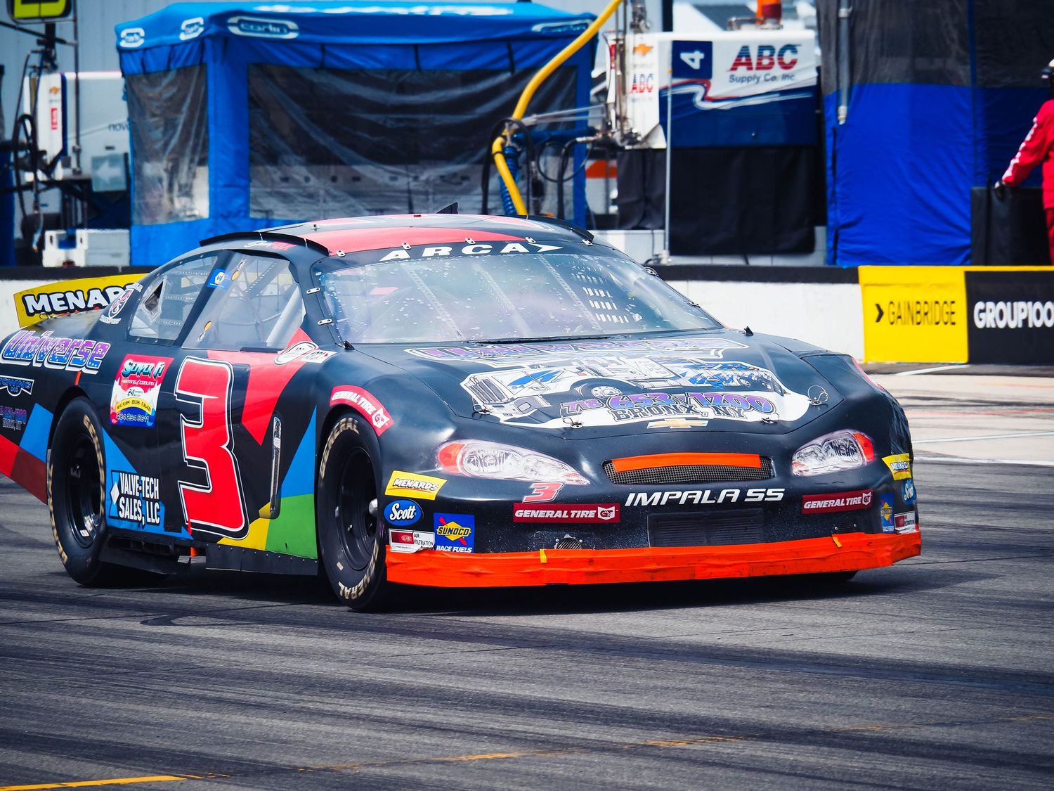 Race cars line up on a track with colorful sponsor logos and sleek aerodynamic designs visible on their bodies.