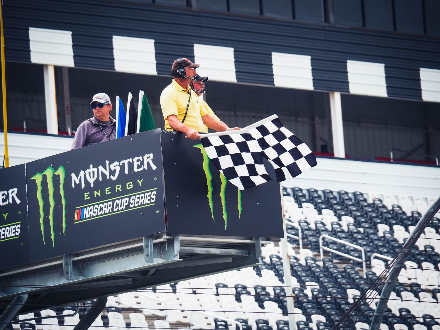 A checkered flag waves over a NASCAR race track with Monster Energy branding visible in the background.