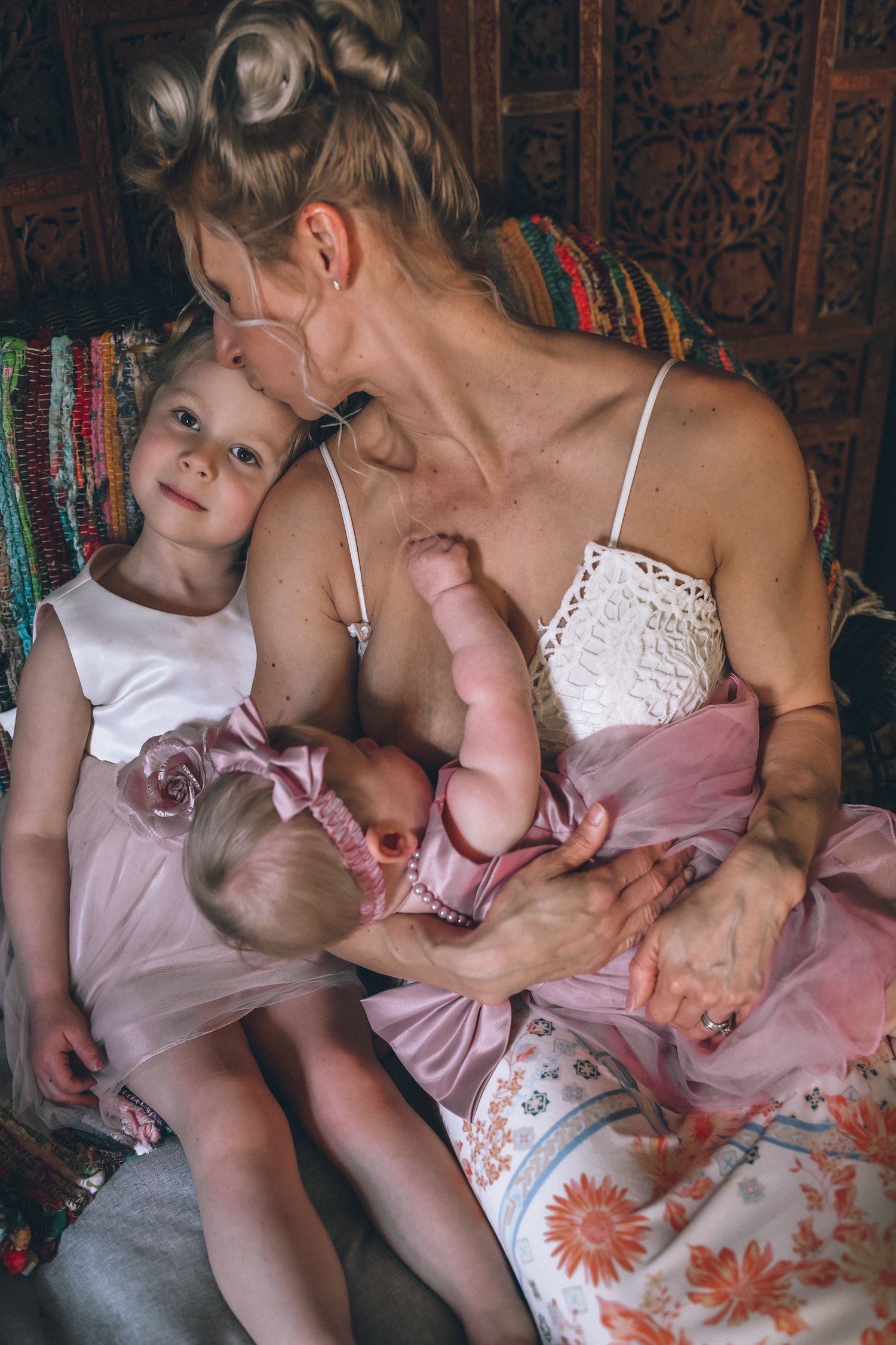 A tender moment between parent and child wearing white and pink clothing while sitting together on a floral patterned couch.
