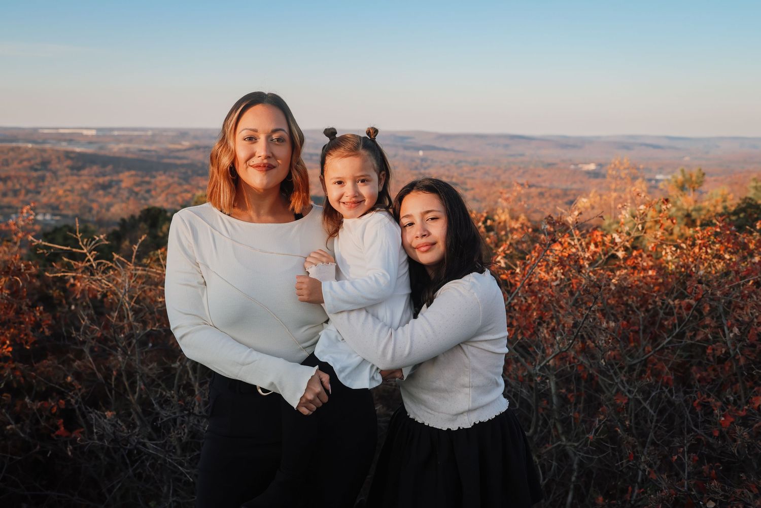 A family enjoys a scenic autumn mountain overlook with colorful fall foliage in the background during golden hour.