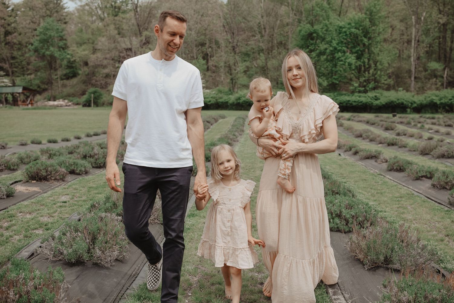 A family poses together in a lavender field wearing coordinated peach and white outfits during a sunny outdoor photoshoot.