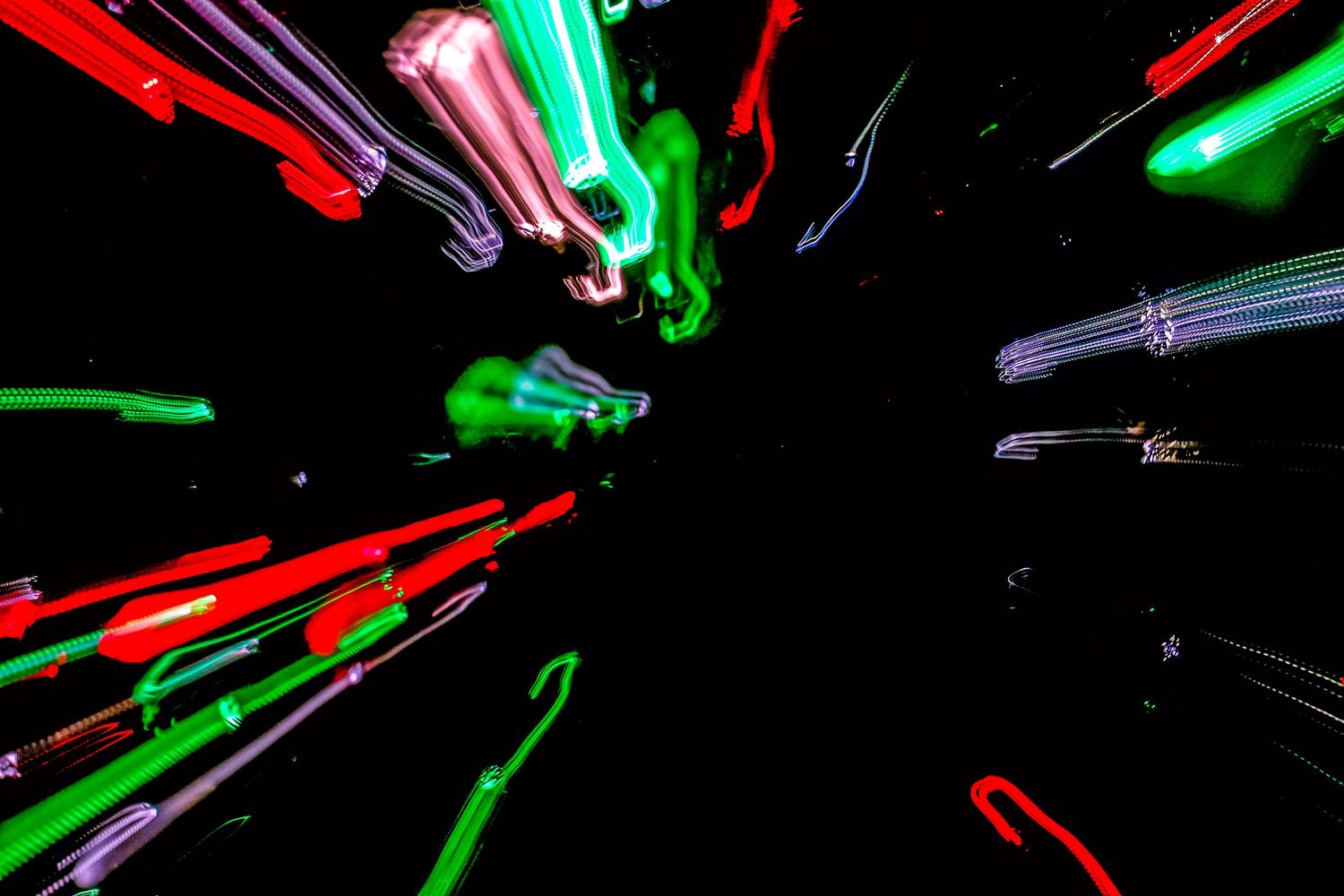 Neon green and red lights streak through darkness in a radial motion blur effect creating an abstract pattern.