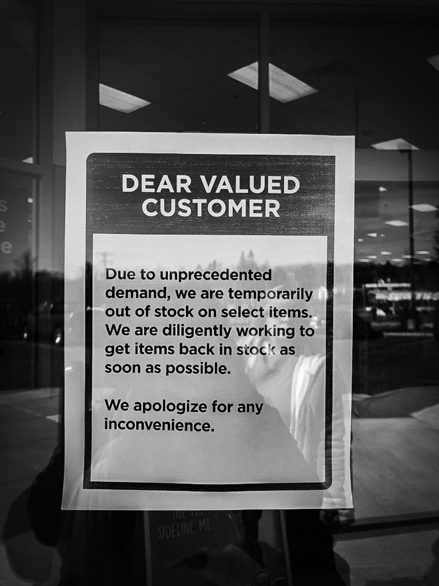 A black and white photo of a store notice apologizing for out-of-stock items due to unprecedented demand.