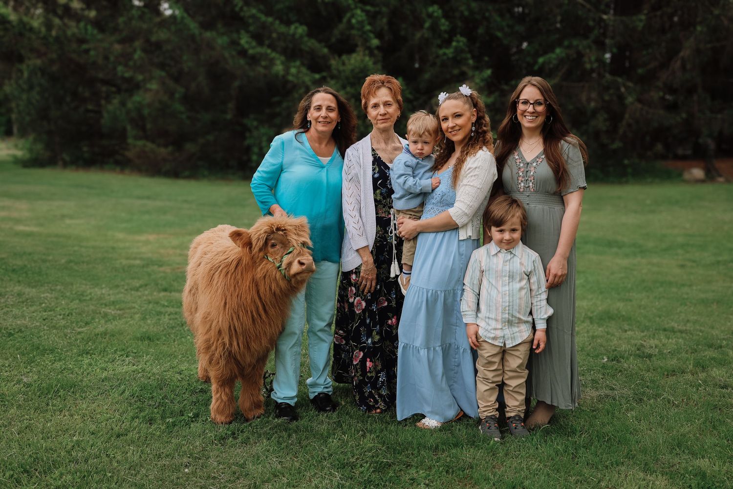 A group of people in coordinated blue and neutral outfits pose together on a grassy lawn for outdoor family portraits.