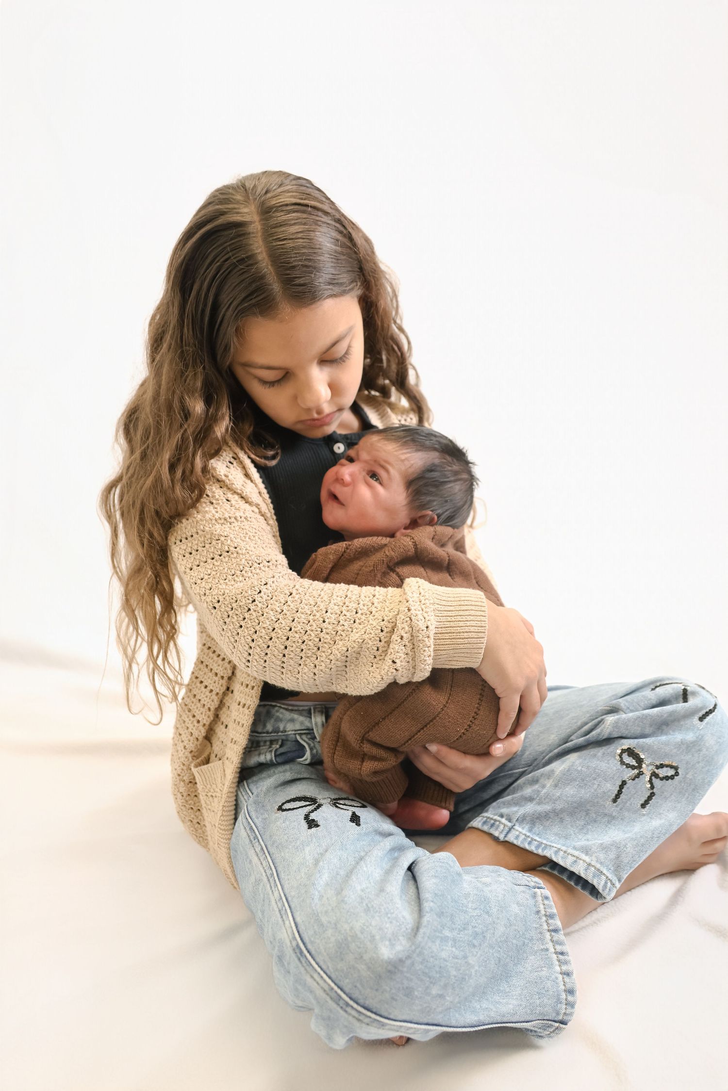 A person wearing a beige sweater and jeans cuddles and embraces someone in a tender moment against a white background.
