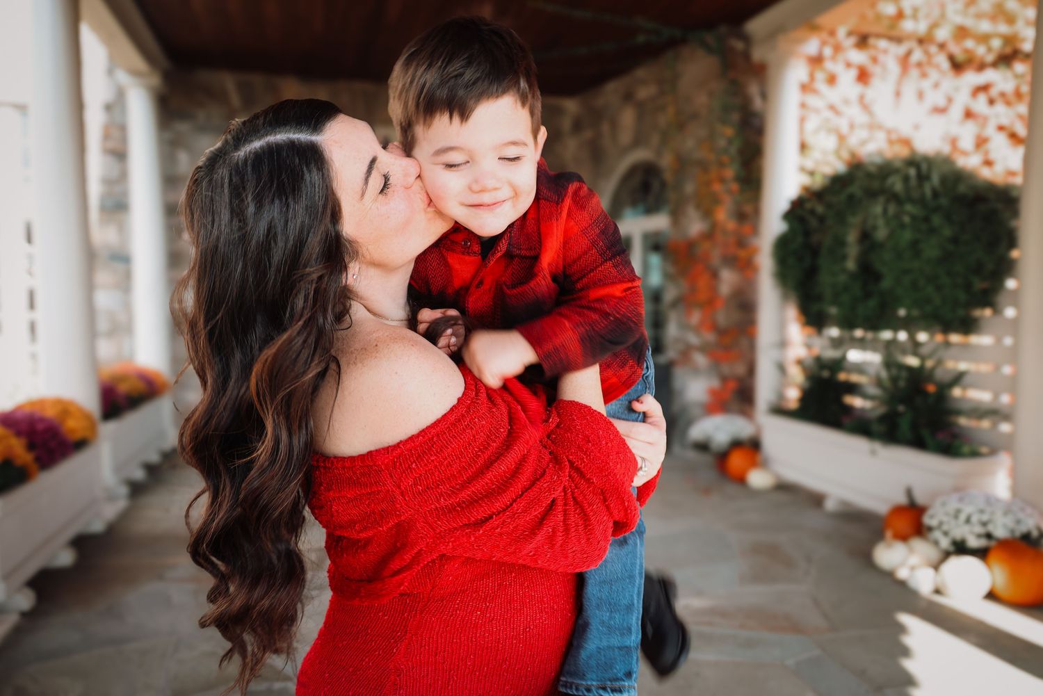 A family wearing red outfits poses together in an outdoor autumn setting with pumpkins and fall decor.